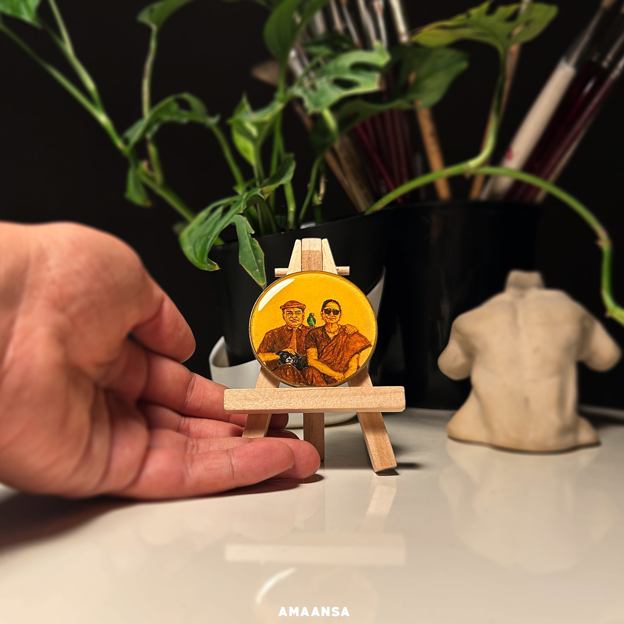 A detailed 5cm diameter miniature painting showcasing a client's great-grandparents with their beloved pets. The grandfather, in a shirt and pants with a European hat, has a black dog on his legs and a green parrot on his shoulder. The grandmother, elegantly dressed in a sari and sunglasses, sits beside him. This custom tabletop showpiece from AMAANSA Fine Arts Studio highlights the challenge of painting small-scale portraits with precision and intimacy, capturing a loving memory of their close relationship