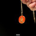 Gold necklace with a red pendant featuring an engraved figure on a black background, branded 'Amaansa'. Custom spiritual locket handpainted Narasimha avatar full color miniature art red background gold foil paper antique-style 18k gold PVD pendant stainless steel chain divine blessing religious keepsake