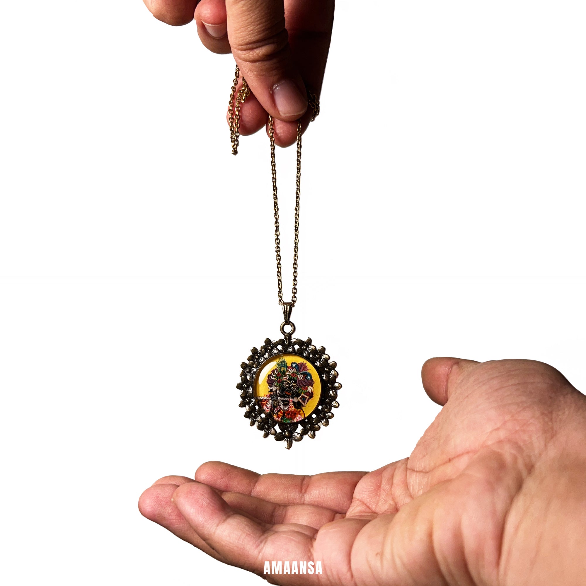 Hand holding a decorative necklace with a pendant against a white. Handpainted semicolor Vrindavan Krishna locket Banke Bihari miniature deity jewelry antique-style chain devotional pendant Lord Krishna floral attire vintage yellow backdrop custom spiritual keepsakebackground