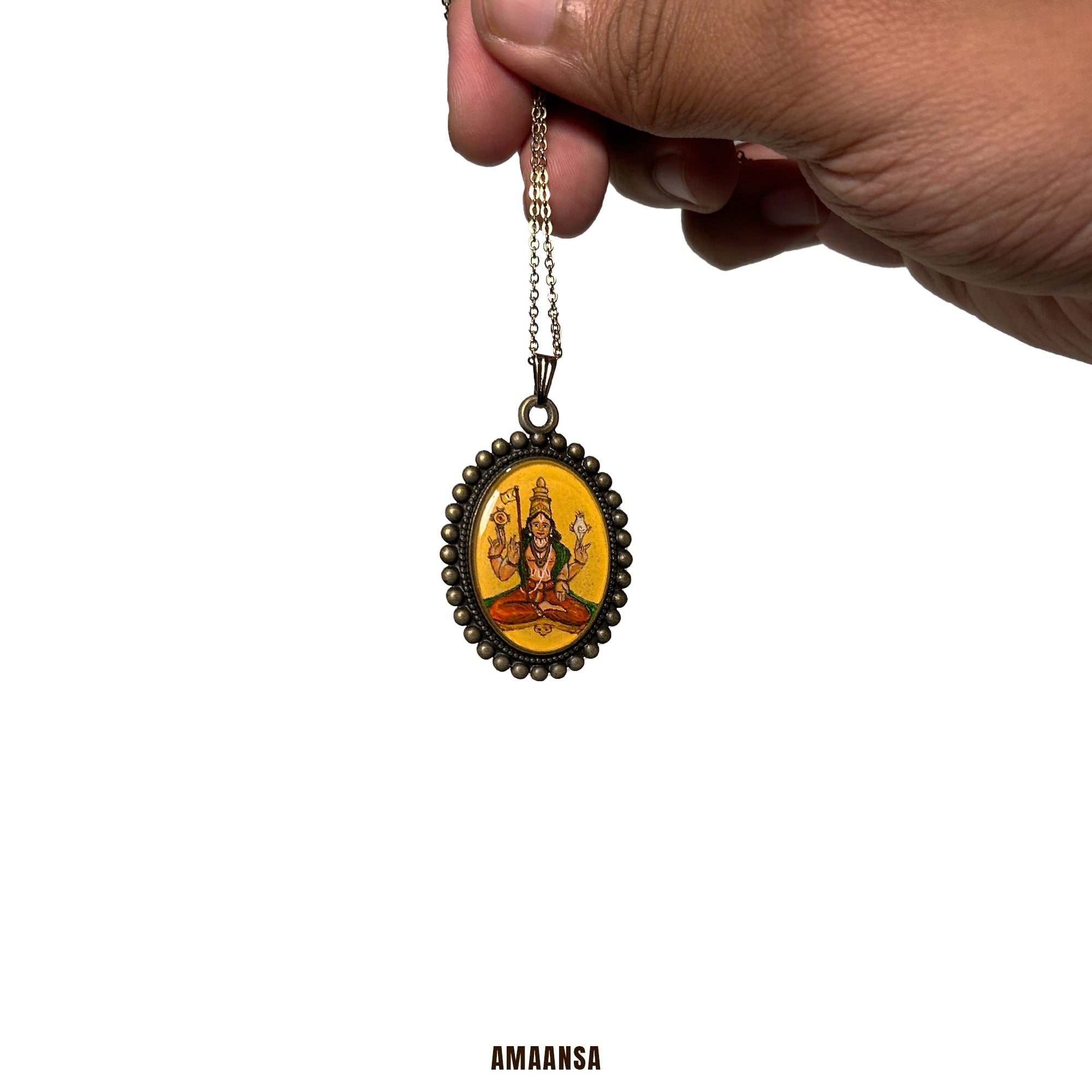 Hand holding a pendant (miniature painting) with a yellow background and 'AMAANSA' branding. Custom deity locket handpainted Sri Vaikhanasa Maharshi semicolor miniature painting full-body guru portrait oval pendant Naples yellow base antique finish devotional jewelry spiritual keepsake heirloom art