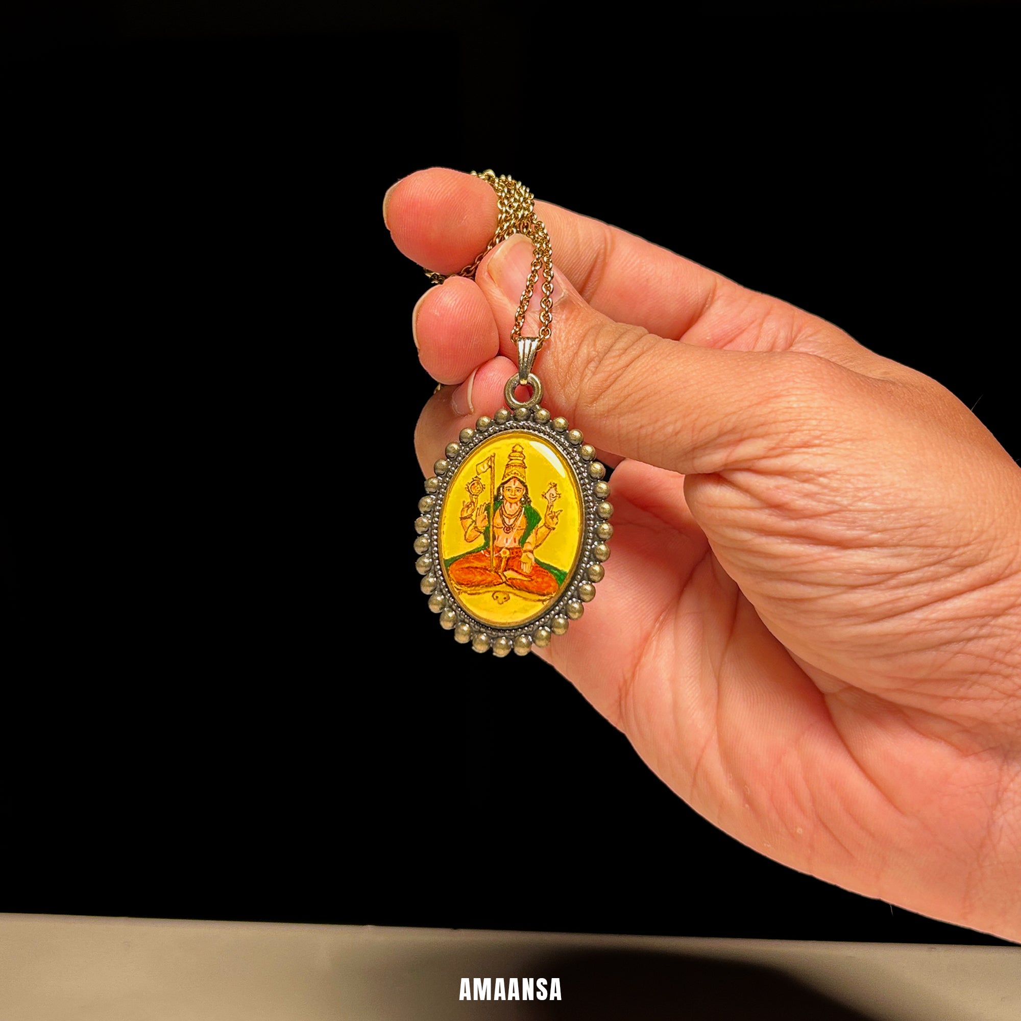 Hand holding a pendant with a religious figure on a black background. Handpainted oval locket Sri Vaikhanasa Maharshi semicolor miniature art vintage style Naples yellow background devotional pendant antique patina chain guru portrait keepsake collectible heirloom piece