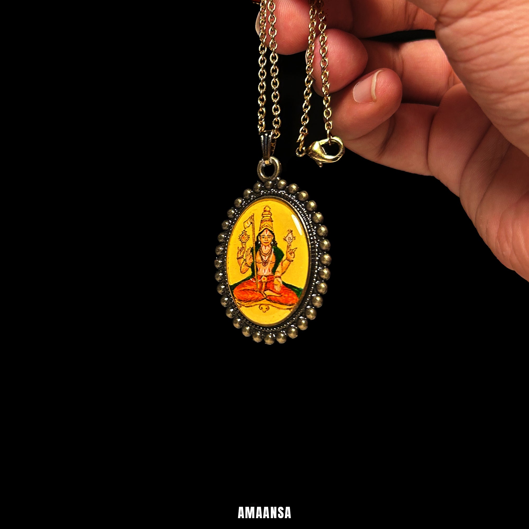 Hand holding a yellow pendant with an engraved design against a black background. Vintage oval pendant Sri Vaikhanasa Maharshi miniature full-body portrait semicolor locket Naples yellow background handpainted devotional jewelry antique-style chain spiritual keepsake heirloom collectible
