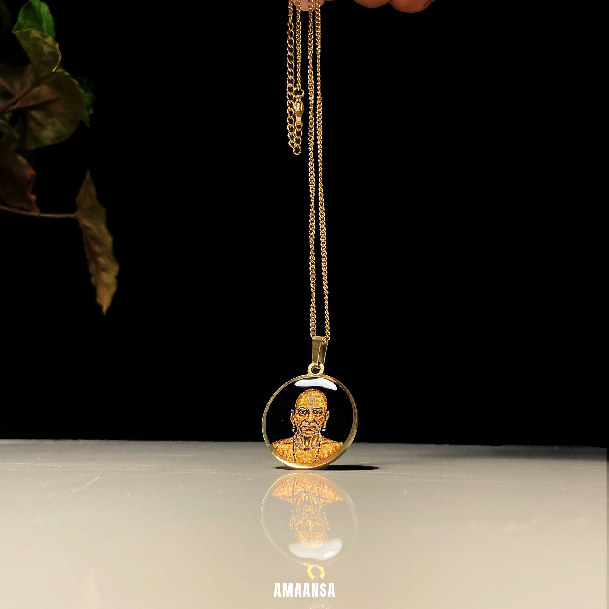 necklace with a pendant featuring a face on a reflective surface. Handpainted monochrome Swami Samarth 18k gold PVD pendant devotional locket gold-tone background spiritual jewelry guru saint portrait keepsake divine protection religious necklace