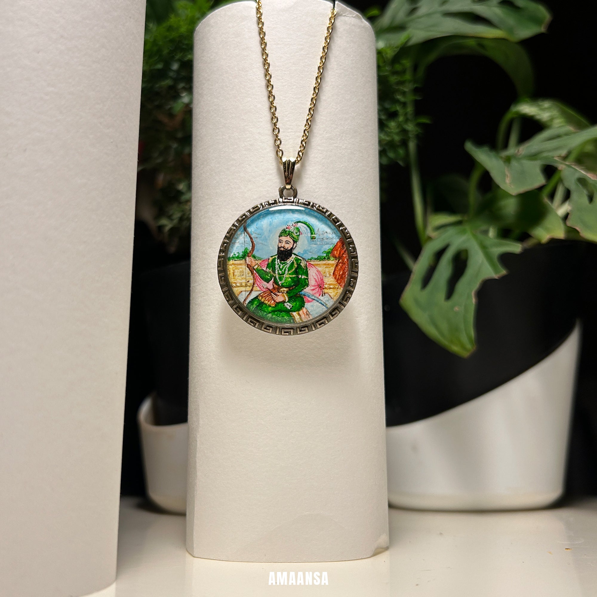 Necklace with a round pendant featuring a colorful painting on a white cylindrical stand with plants in the background. Custom deity locket handpainted Guru Gobind Singh full color vintage pendant spiritual jewelry Sikh god coin religious necklace divine blessing devotional chain Mughal miniature art any deity made to order AMAANSA