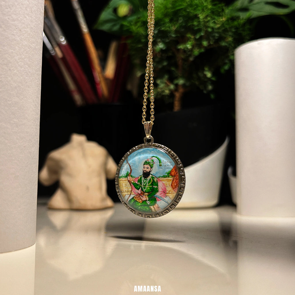Guru Gobind Singh hand‑painted miniature pendant on chain, devotional and heritage jewelry photographed in creative studio setting.