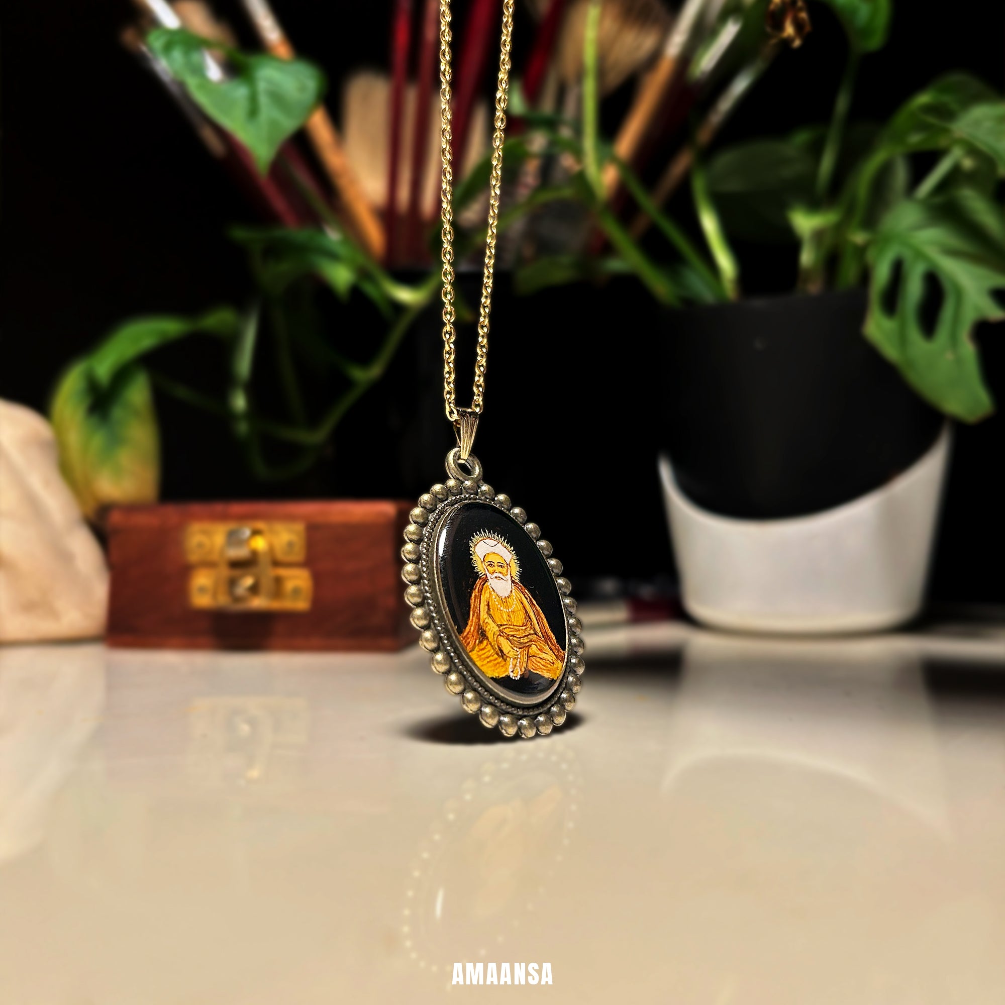 Necklace with pendant featuring a portrait on a reflective surface with plants in the background. Guru Nanak pendant vintage style handpainted miniature locket Sikh deity jewelry custom spiritual coin divine protection religious necklace devotional keepsake meditative pose black background AMAANSA artistry vintage yellow hues