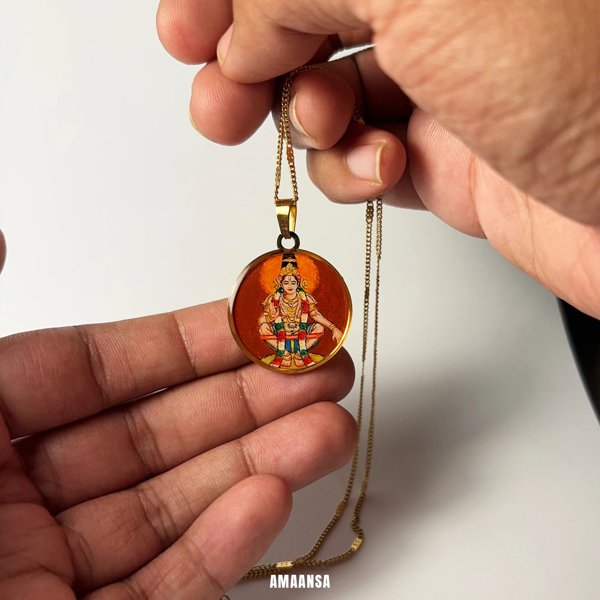 Hand holding a suspended 18k gold plated round Lord Ayyappa pendant featuring an engraved design on a white background, hand‑painted miniature worn during pilgrimage and daily prayer.
