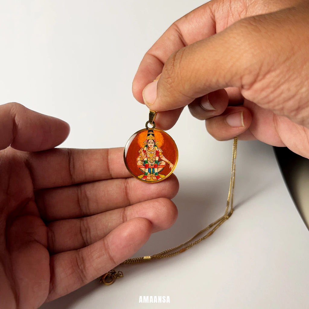 Hand holding a gold necklace with a pendant featuring a miniature handpainted painting of Ayyappa on a white background. devotional necklace for Sabarimala devotees