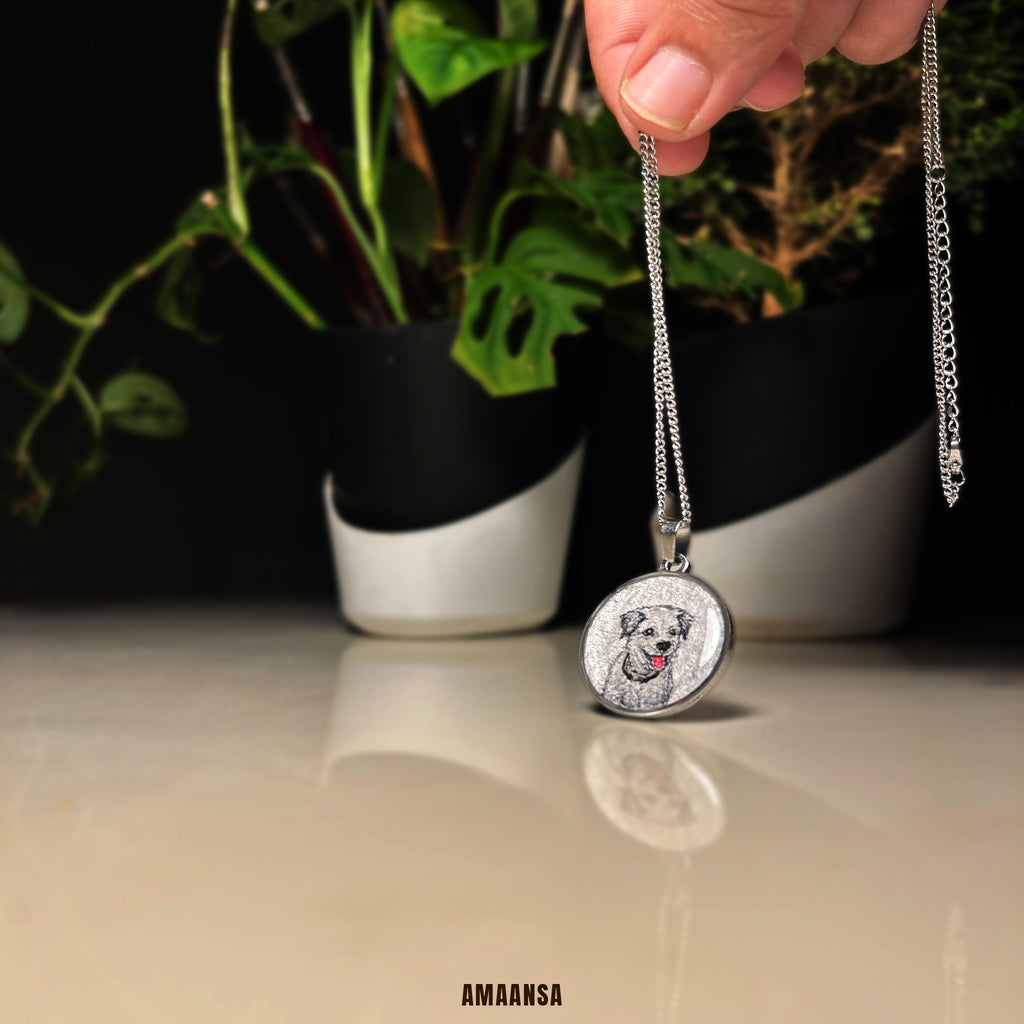Silver necklace with a pendant featuring a dog's face, held above a reflective surface with plants in the background. Premium beloved memorial locket handpainted pet portrait silvery white finish custom dog jewelry memorial pendant miniature art pet tribute commissioned keepsake furry family remembrance wearable nostalgia collectible