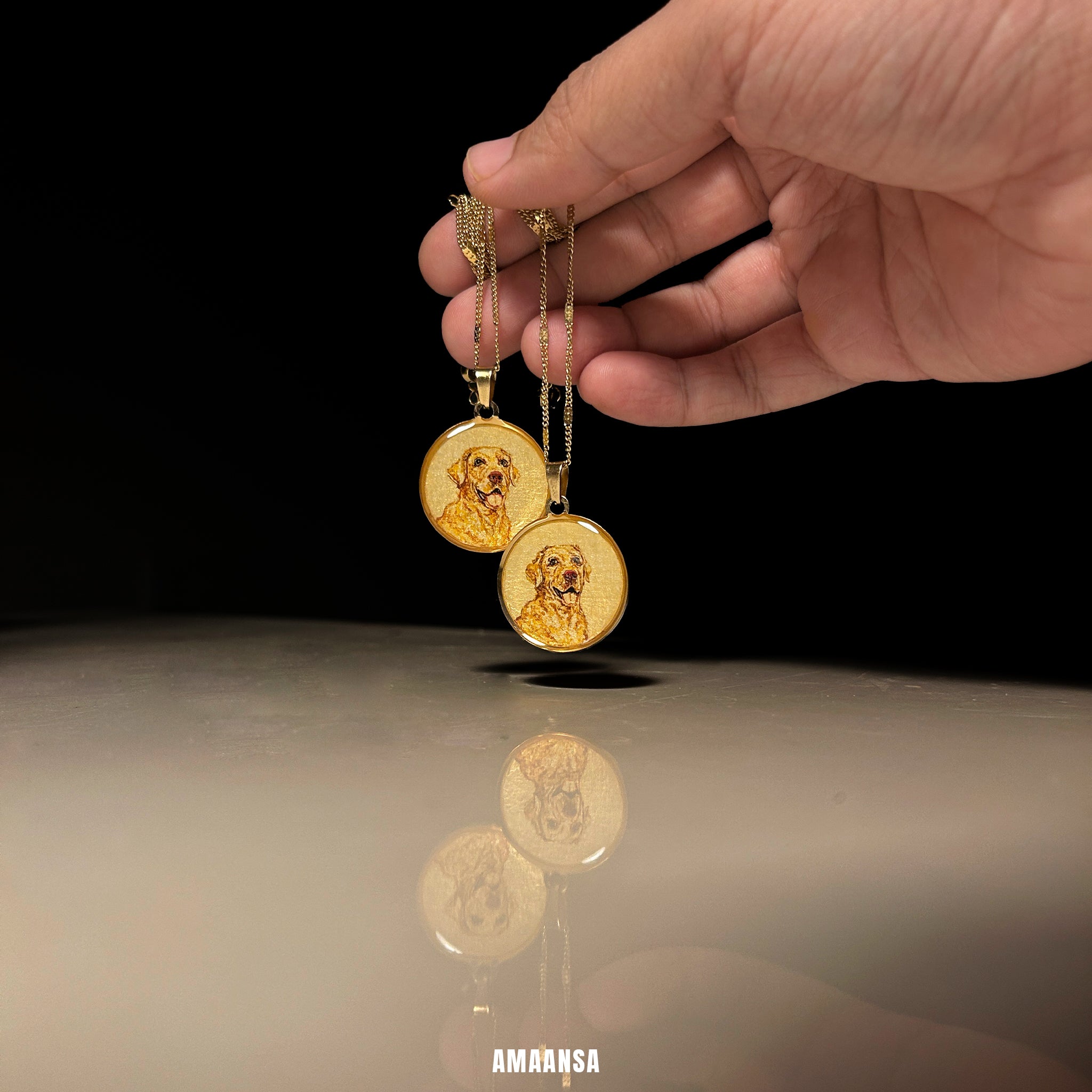 Gold dog pendant necklaces held by a hand on a reflective surface with a black background. Custom pet Canine-specific memorial jewelry set Golden Retriever portrait pendants handpainted miniature art 18k gold PVD premium pet lockets dog memorial keepsake commissioned remembrance gift dual necklace furry family tribute