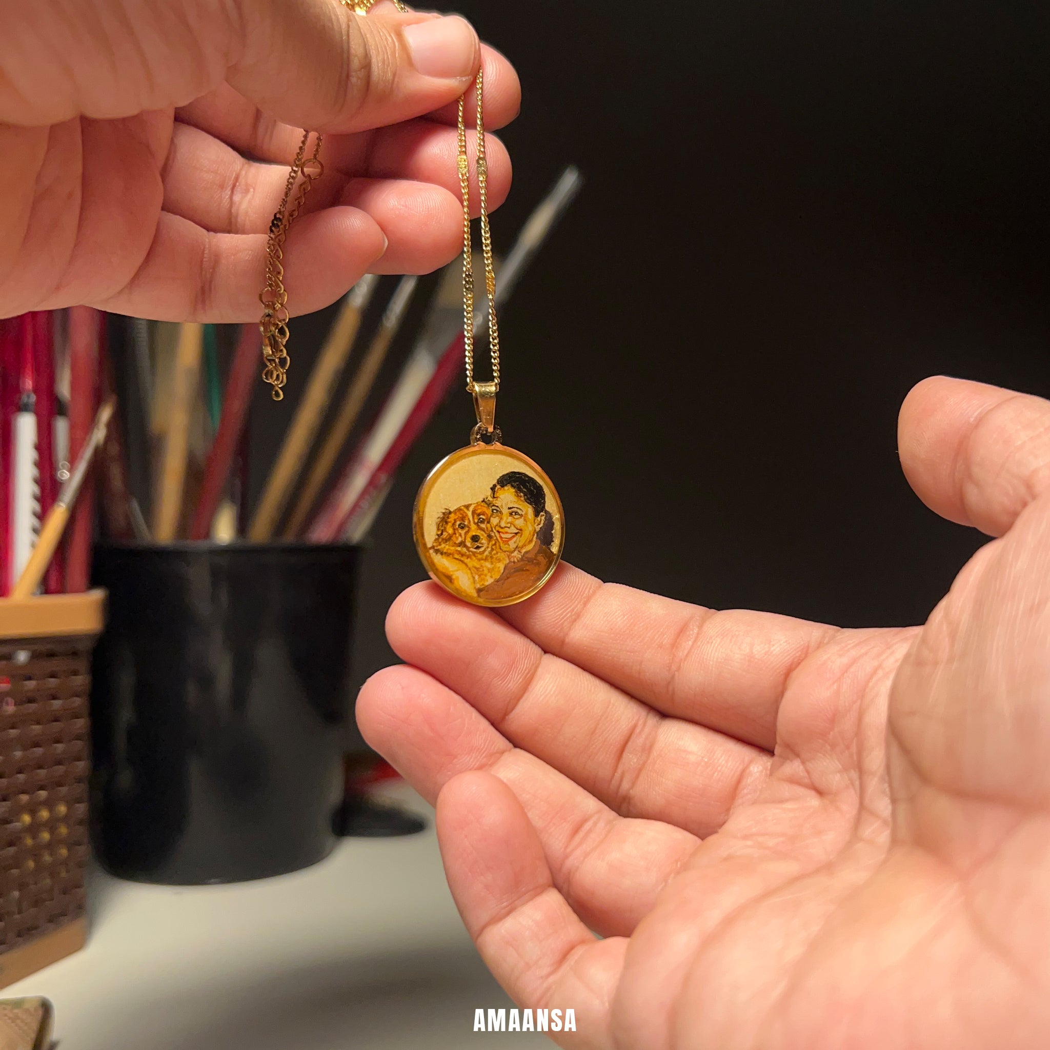 Gold plated pendant held by a hand with a blurred background. Custom pet memorial pendant handpainted two-face portrait mother holding Pomeranian 18k gold PVD premium dog jewelry personalized keepsake commissioned daughter gift furry companion remembrance AMAANSA artistry memorial locket
