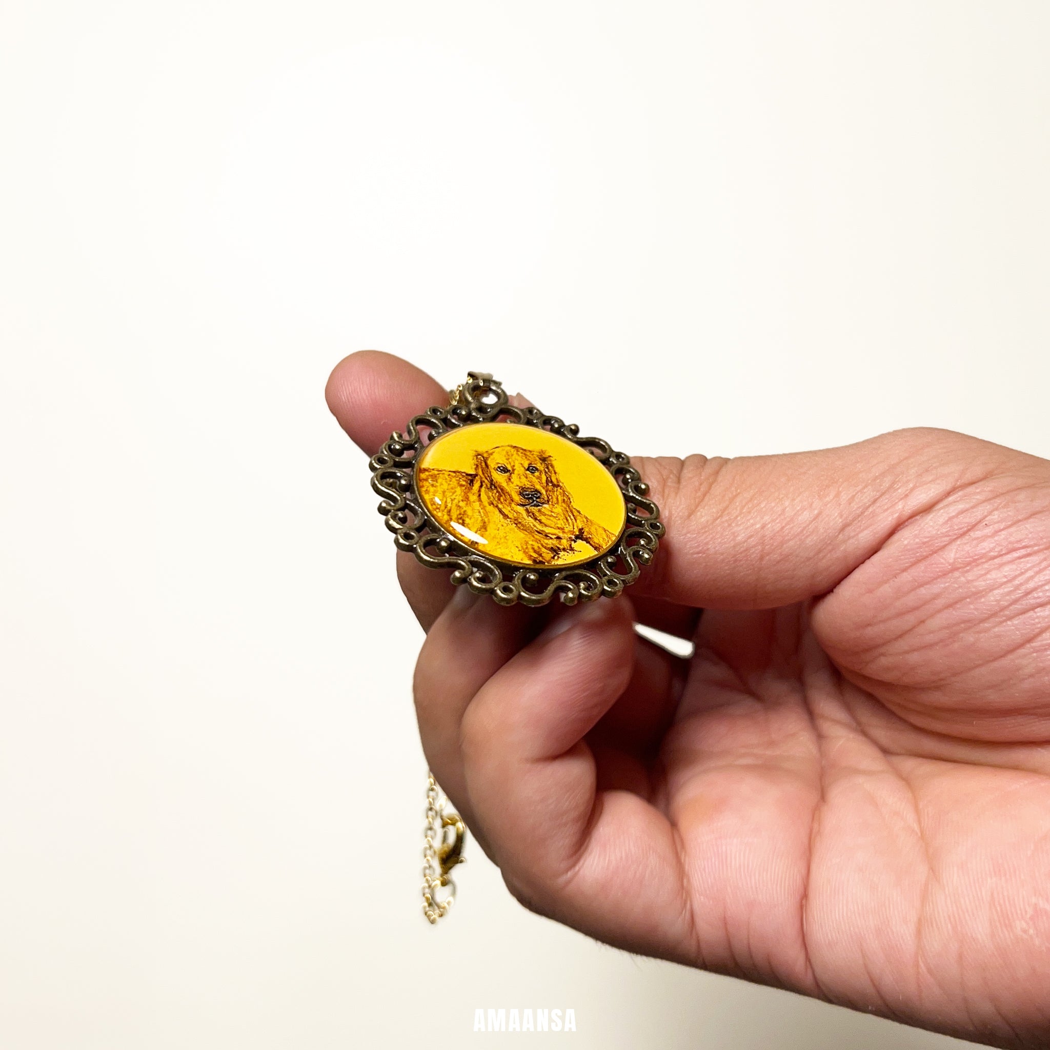 Hand holding a pendant with a yellow center dog painting inside and intricate design on a white background. Handpainted vintage pet portrait locket custom dog memorial jewelry ornate oval pendant antique finish beloved companion keepsake personalized tribute miniature art vintage style collectible furry family remembrance