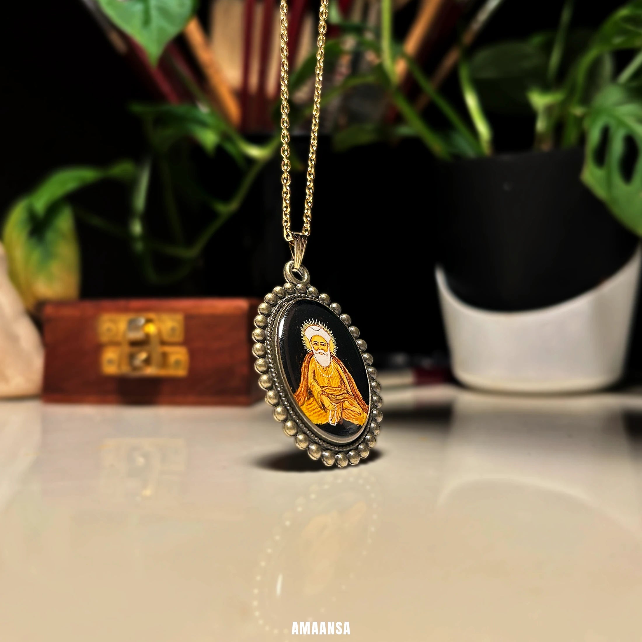 Side view of Guru Nanak pendant lying on surface, devotional necklace casting soft reflection with plants in the background