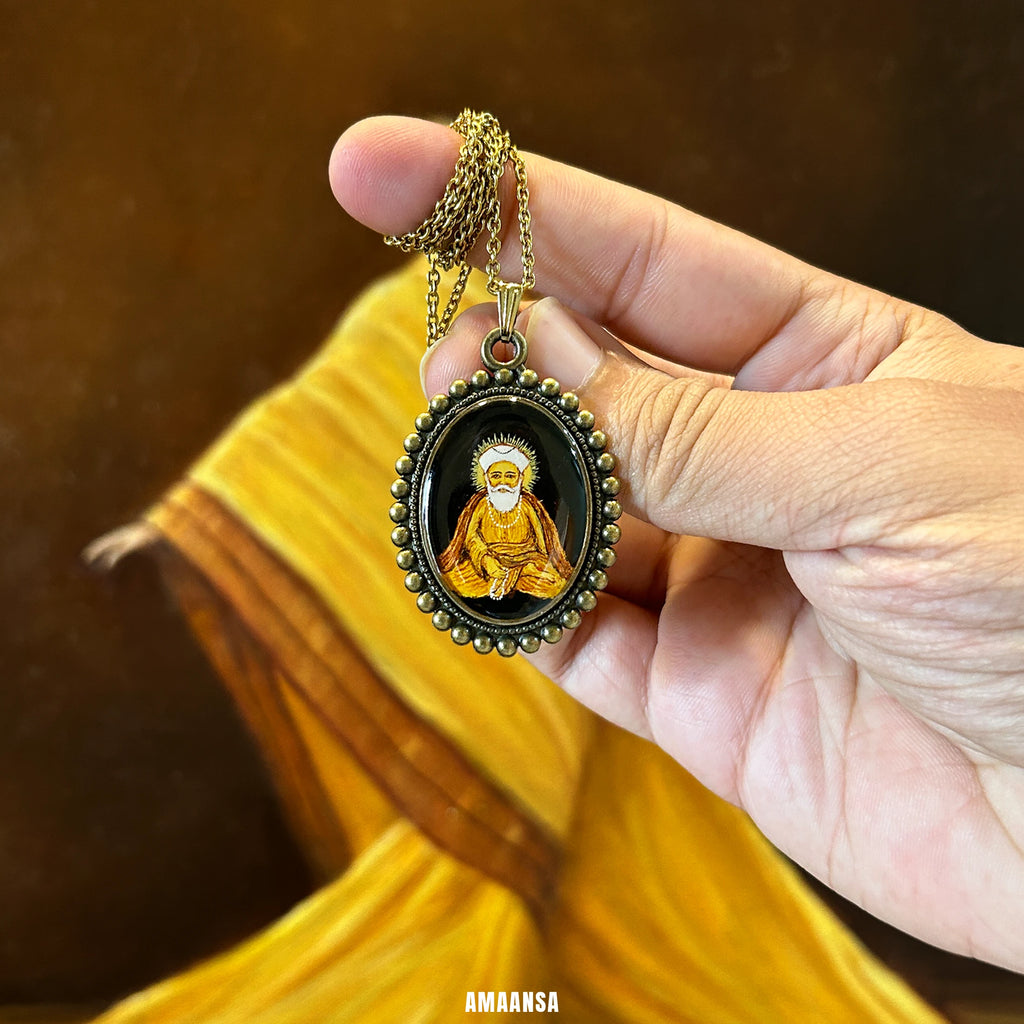 Guru Nanak pendant held in hand, hand‑painted miniature worn as daily remembrance of teachings, against a blurred background.