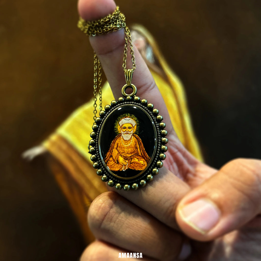 Hand holding a necklace with a pendant featuring Guru Nanak pendant held in hand in orange robes., hand‑painted miniature worn as daily remembrance of teachings.
