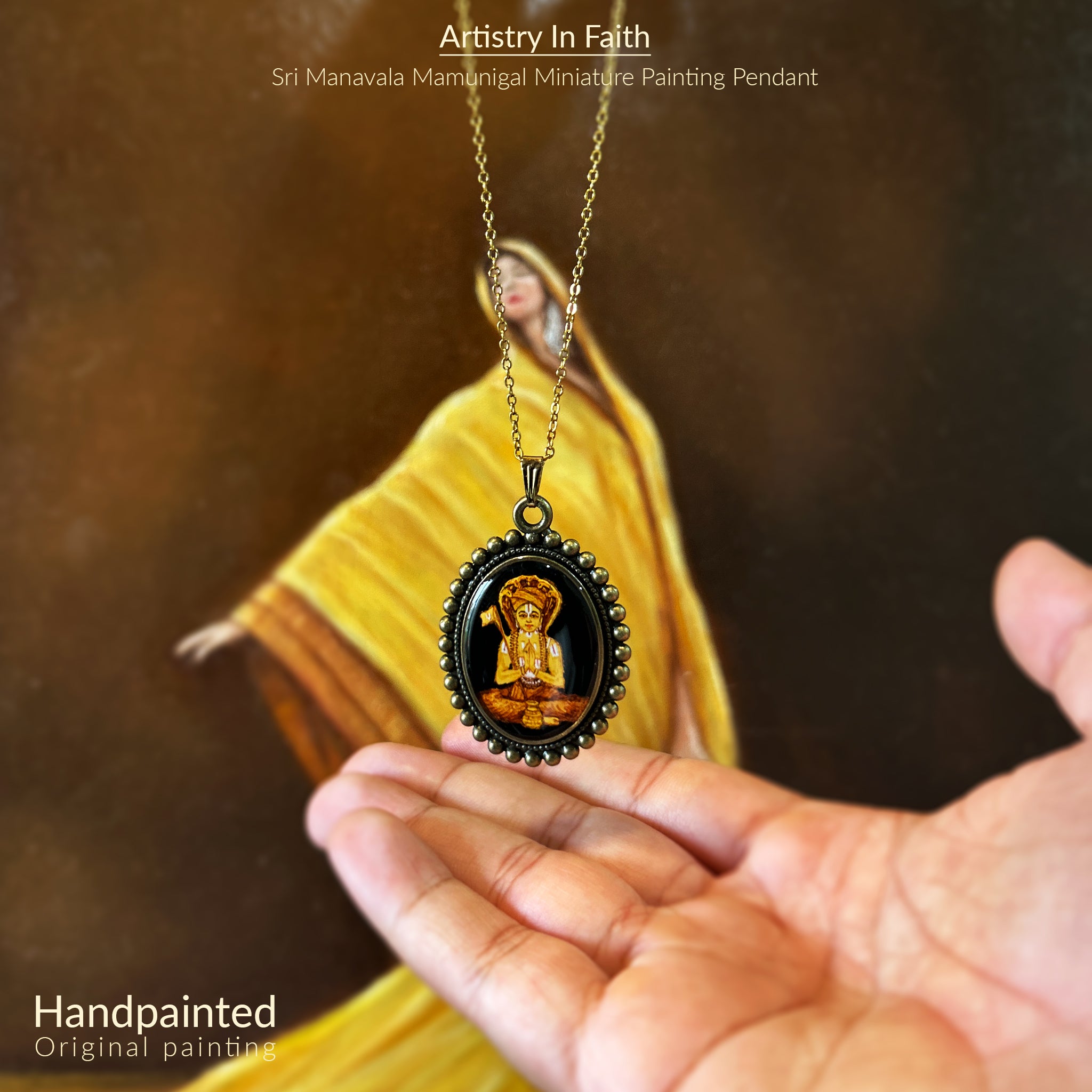 AMAANSA's blessed oval pendant (31x23mm) featuring Sri Manavala Mamunigal's complete portrait with sacred attributes. His crown adorned with six serpents and victory flag painted in rich golden hues, framed by Vintage Pearl Border in antique brass finish. Pendant gracefully suspended above open palm with antique gold colored chain flowing, photographed against artist's draped yellow fabric. Crystal-clear sealant protects this spiritual keepsake's divine essence.