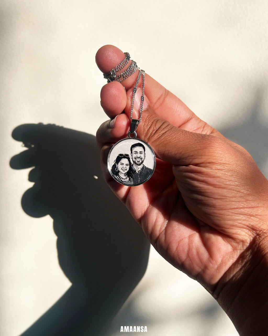 Hand holding a round silver toned pendant with a miniature painting of a couple against a blurred background