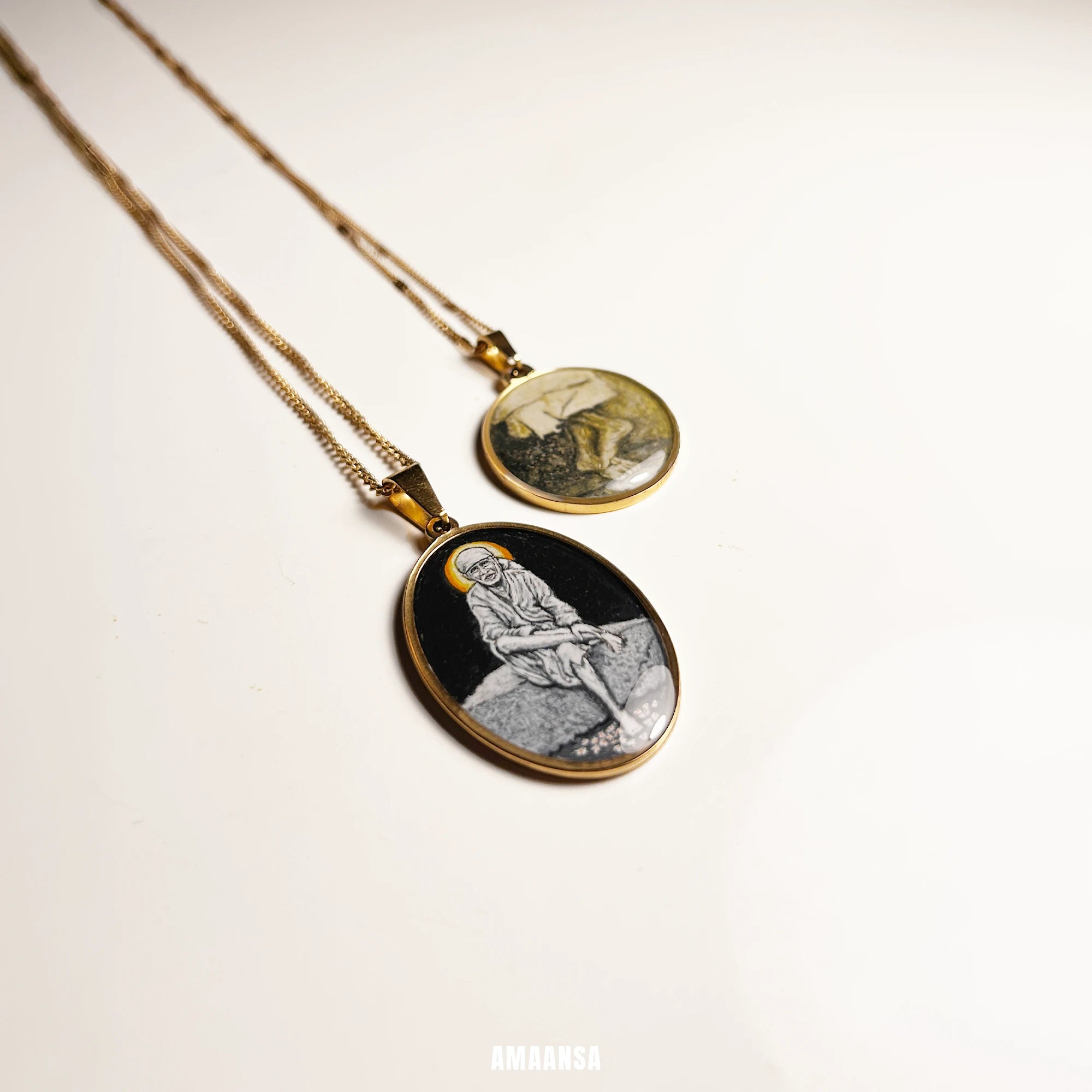Two gold necklaces with Sai baba and Sai baba charan painting inside oval pendants on a white reflective background