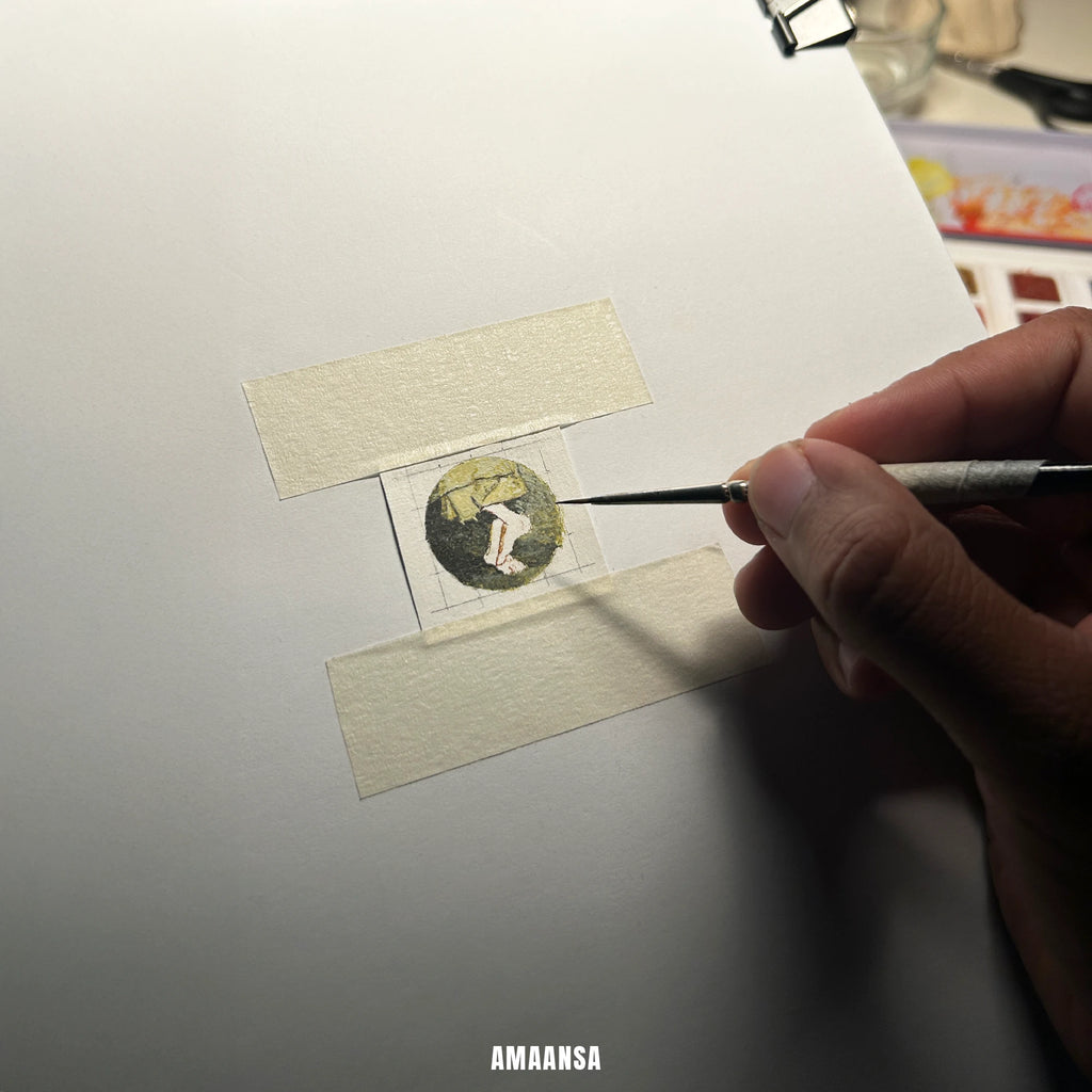 Miniature painting of Sai Baba charan in progress on taped paper, early layers of sacred feet artwork for devotional pendant.