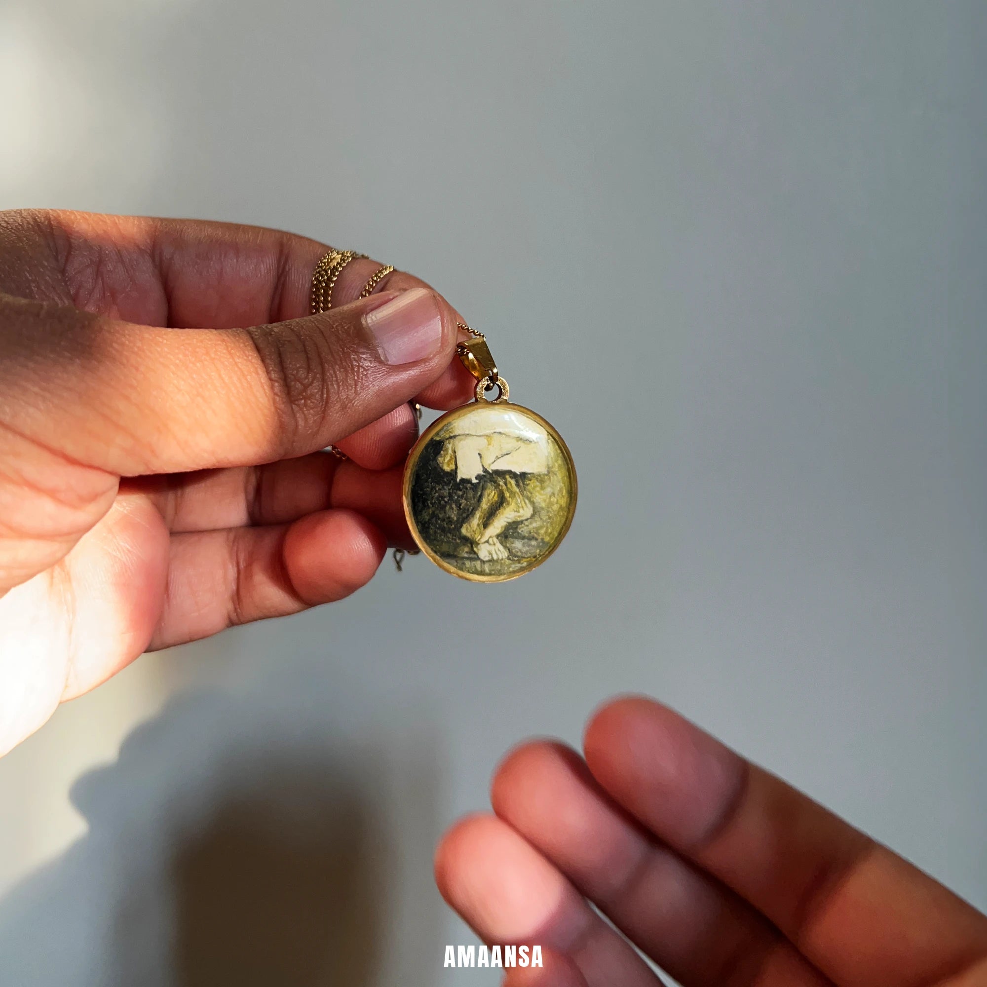 Hand holding a round pendant with a painting of Sai Charan (feet) against a neutral background