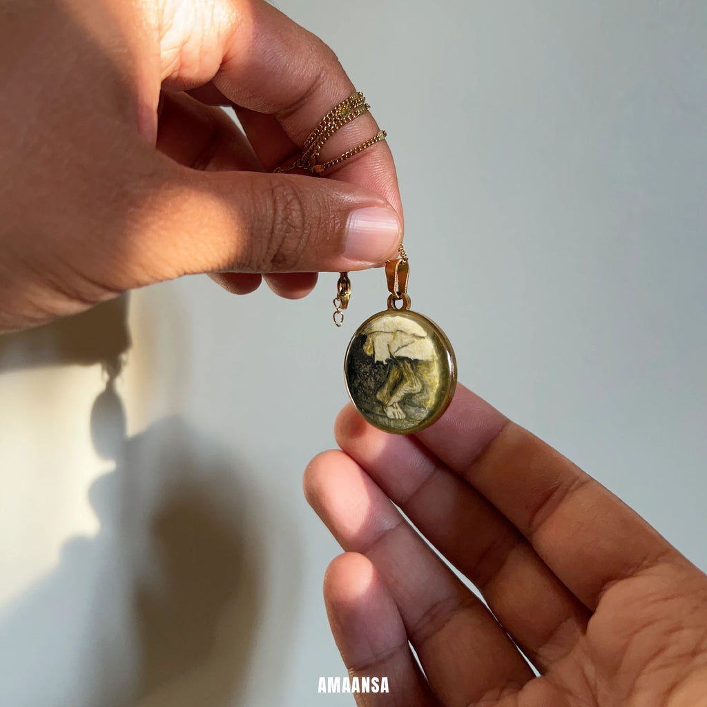 Hand holding a pendant with a detailed design against a neutral background. Sai Baba charan 18k gold‑plated pendant with polished dome and sacred feet miniature, devotional necklace centred on clean background.