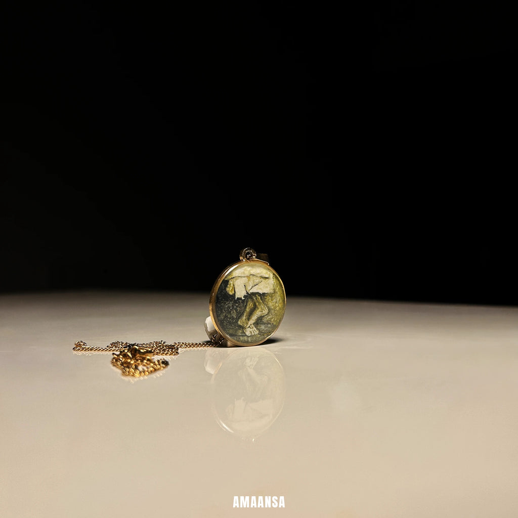 Sai Baba charan 18k gold‑plated miniature pendant resting on smooth surface with chain, devotional necklace styled for spiritual gift. Gold pendant on a reflective surface with a dark background