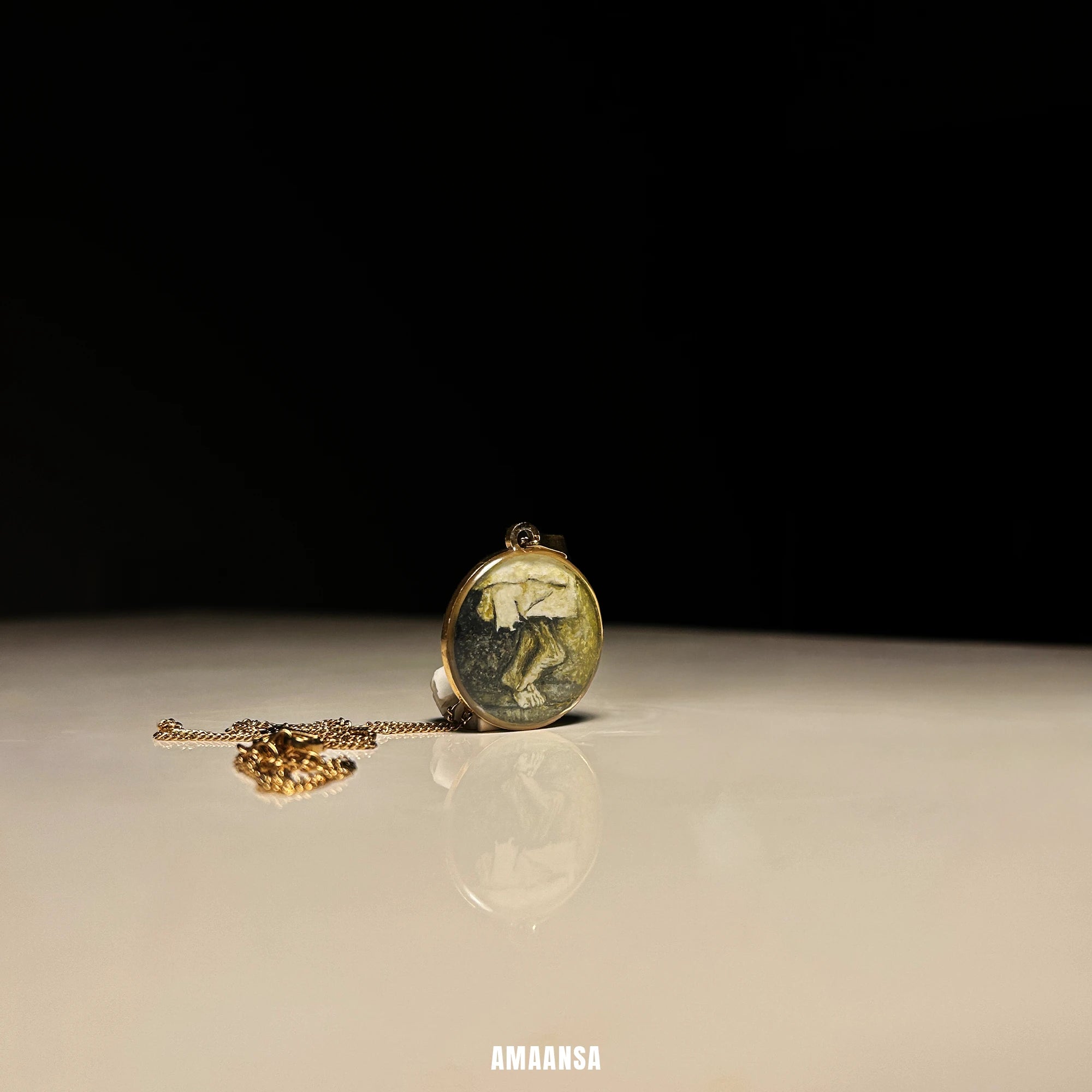 Sai Baba charan 18k gold‑plated miniature pendant resting on smooth surface with chain, devotional necklace styled for spiritual gift. Gold pendant on a reflective surface with a dark background