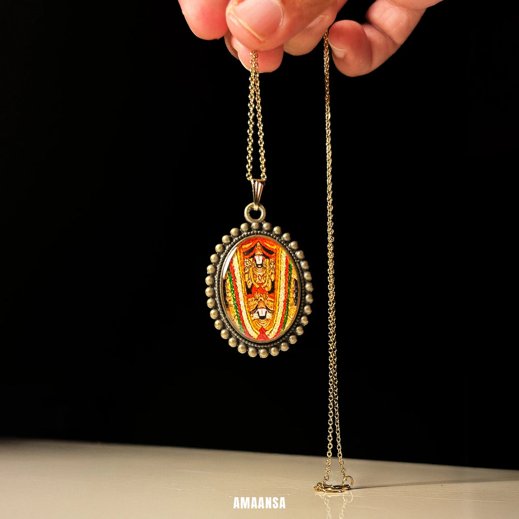 Venkateswara Swamy antique gold‑tone oval miniature pendant on chain, hand‑painted devotional jewelry photographed on sunlit stone background.