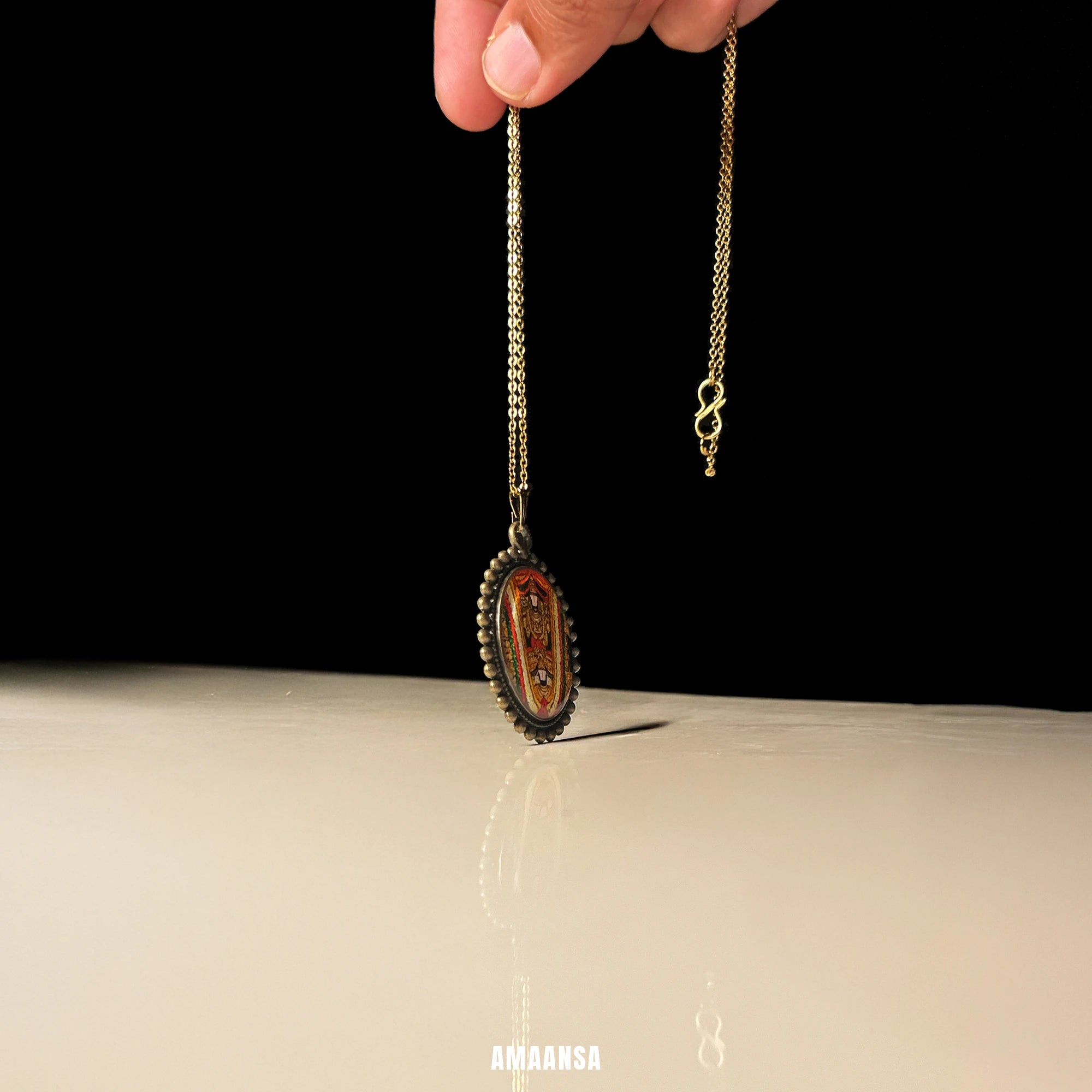 Angled close‑up of Sri Venkateswara Swamy hand‑painted miniature pendant, antique gold‑tone oval frame on chain against clean studio backdrop.