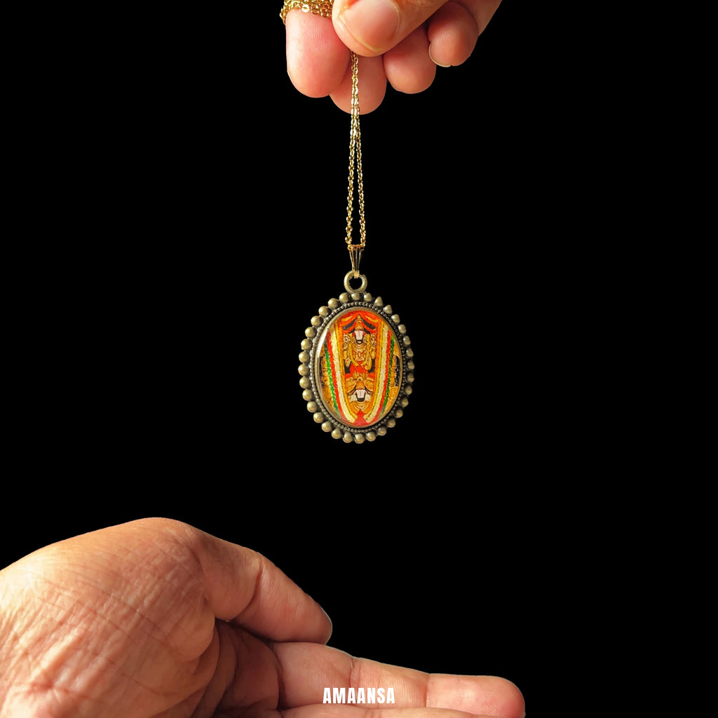 Hand holding a Sri Dwaraka Tirumala Venkateswara Swamy gold‑tone oval miniature pendant hanging from long chain, devotional necklace displayed at full drop, with intricate designs against a black background