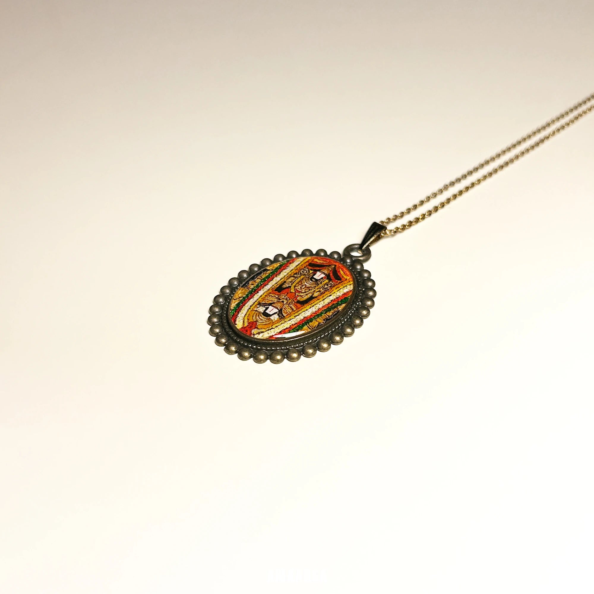 Sri Dwaraka Tirumala Venkateswara Swamy gold‑tone oval miniature pendant on chain above reflective surface, devotional necklace in product spotlight on a beige background