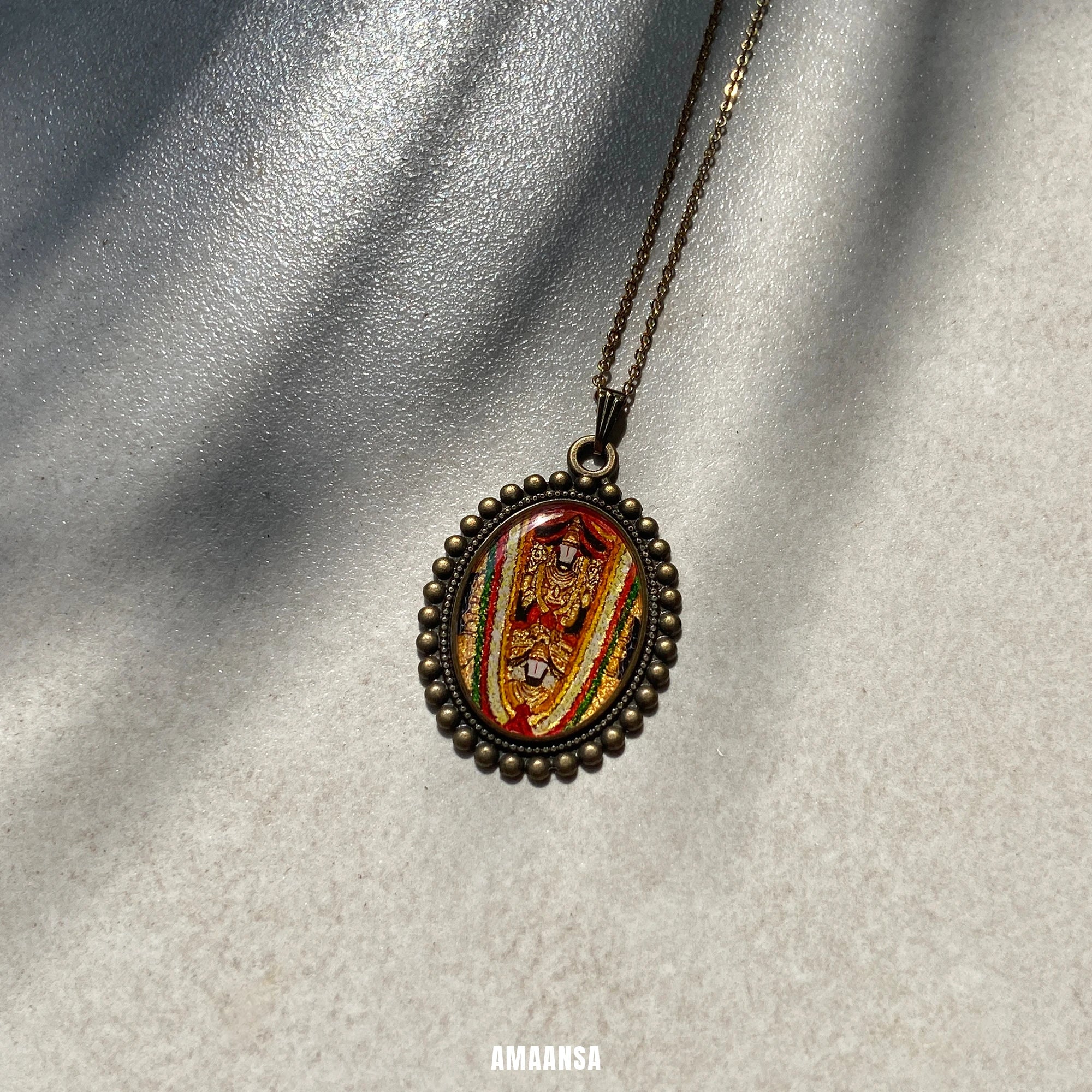 Sri Dwaraka Tirumala Venkateswara Swamy gold‑tone oval miniature pendant on chain on a textured gray background,.