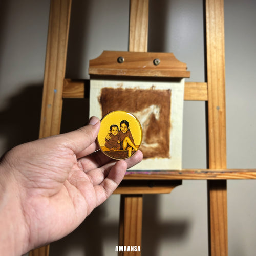 Hand holding a round yellow object with a printed design in front of a wooden easel (oil painting). Custom miniature family portrait two figure tabletop display handpainted sibling art toddler childhood memory wooden easel stand desk accessory office decor brother commissioned sister gift AMAANSA studio background