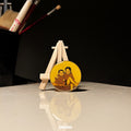Small round painting on a wooden easel with brushes in the background. Custom tabletop miniature portrait two figure sibling art professional photography handpainted family keepsake wooden stand desk display personalized collectible brother sister childhood memory office decoration