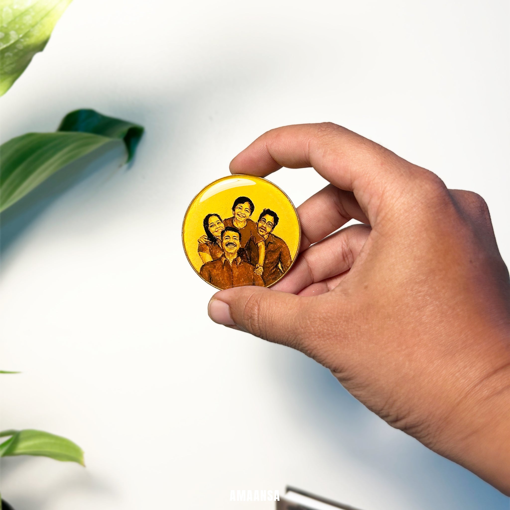 Hand holding a yellow button with a familyminiature painting against a light background. Custom tabletop miniature portrait family of four parents two sons handpainted family art wooden easel stand desk display complete family unit vintage style collectible keepsake emotional bonding treasure
