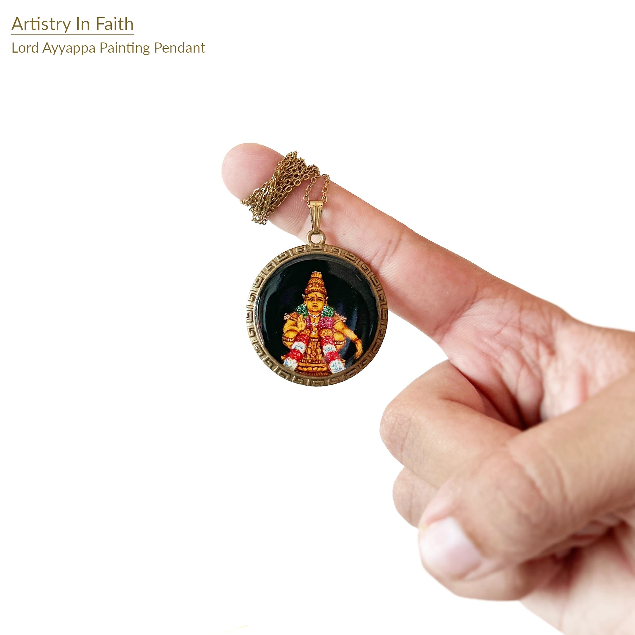 Finger holding a pendant with Lord Ayyappa painting on a white background, showing crown and ornaments, devotional necklace detail shot.