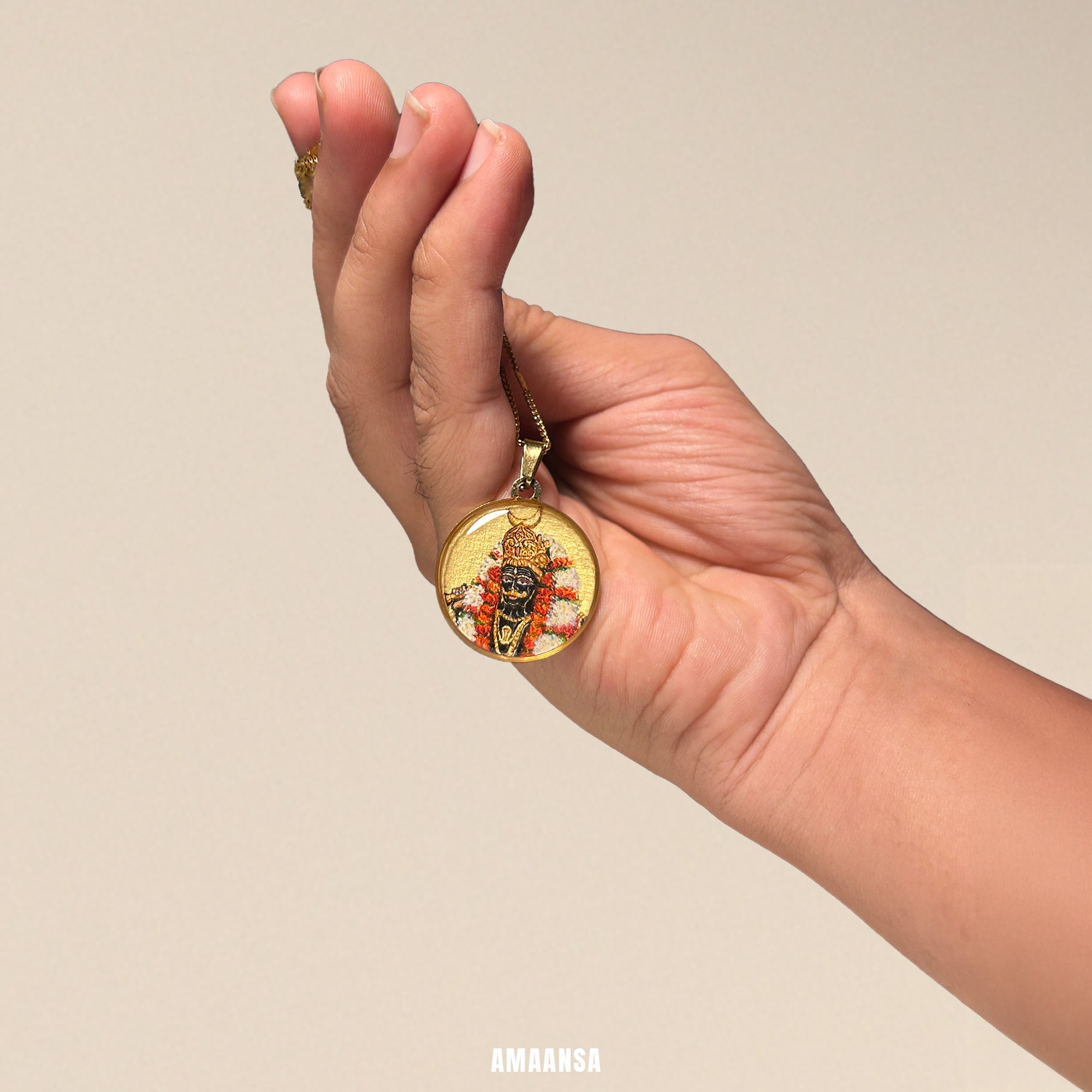 Hand holding a gold necklace with a pendant against a beige background. Handpainted Bhairon lord half-figure locket semicolor miniature art 18k gold PVD pendant stainless steel chain devotional jewelry red orange floral adornment spiritual talisman heirloom piece