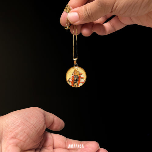 Gold pendant with intricate design held by a hand against a black background. Handpainted Kalabhairava half-body miniature semicolor locket 18k gold PVD chain devotional pendant red orange garland white florals spiritual jewelry divine protection keepsake