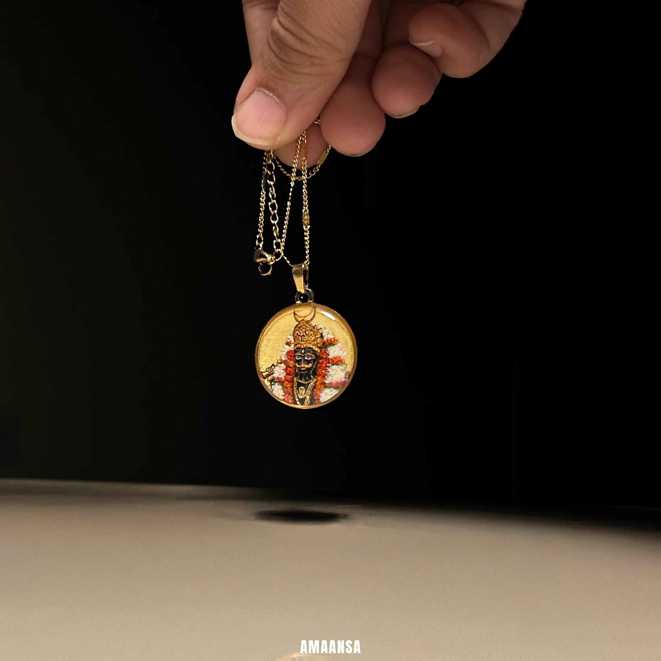 Kaal Bhairava 18k gold‑plated miniature portrait pendant on reflective surface, devotional jewelry highlighting protective deity and floral halo.