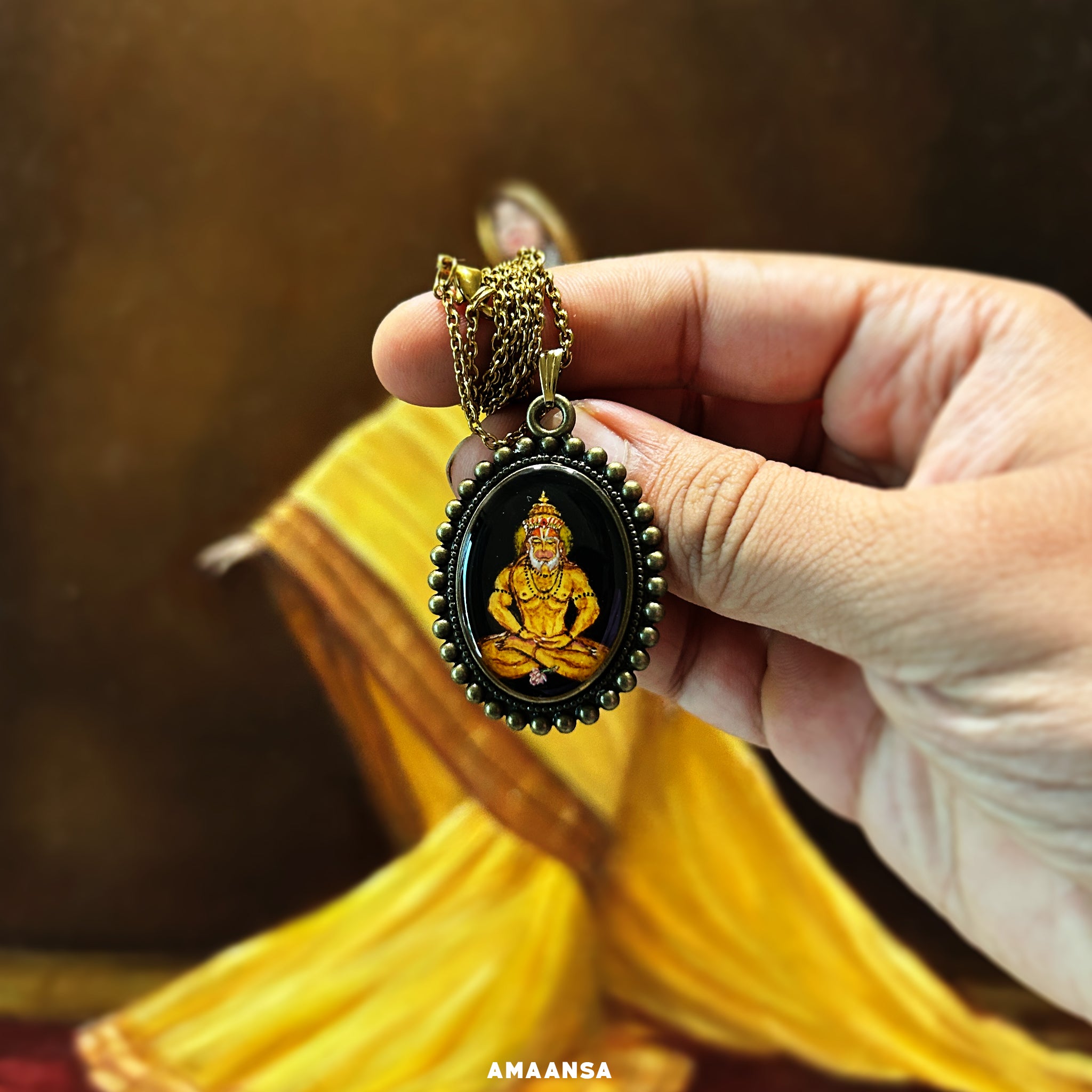 An intricately detailed miniature pendant from the 'Artistry in Faith' collection, featuring Lord Hanuman in a meditative pose. The painting, set on a 26mm x 32mm oval metal base, shows Hanumanji with a divine glow behind his head, wearing a crown and seated with hands near his legs in meditation, a small flower at his feet. The pendant's black background contrasts with vintage yellow hues. The outer rim features a classic moti-style design, and the pendant comes with a chain, making it a wearable art piece