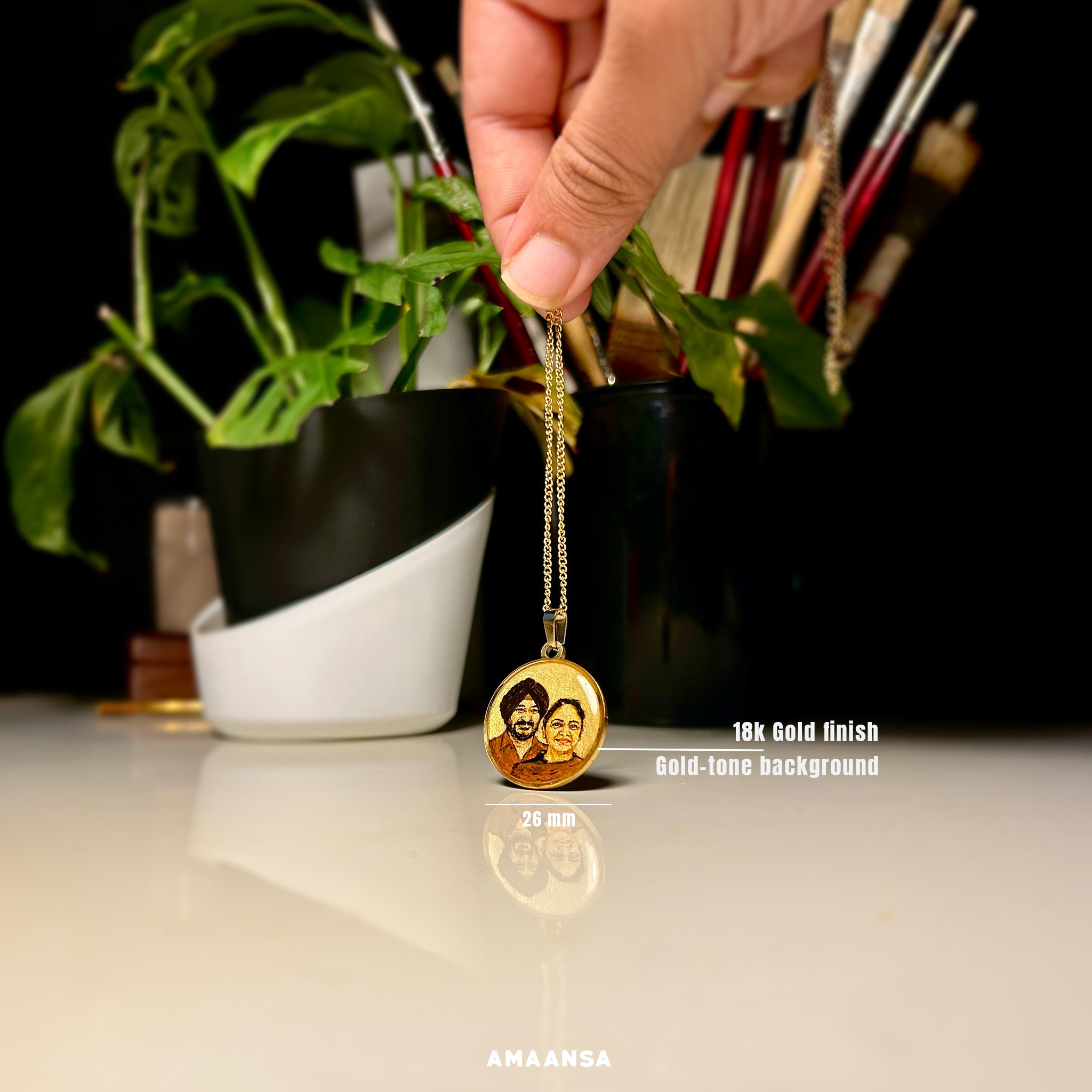 Bespoke miniature artistry merges cherished memories - 26mm pendant showcasing parents' united portrait crafted from separate photographs, father's distinguished turban and gentle smile beside mother's radiant expression, expertly harmonized by artist Abhinav in rich sepia tones against luminous gold backdrop, elegantly suspended from 18k gold PVD plated chain held against vibrant monstera leaves, reflecting the pendant's delicate scale