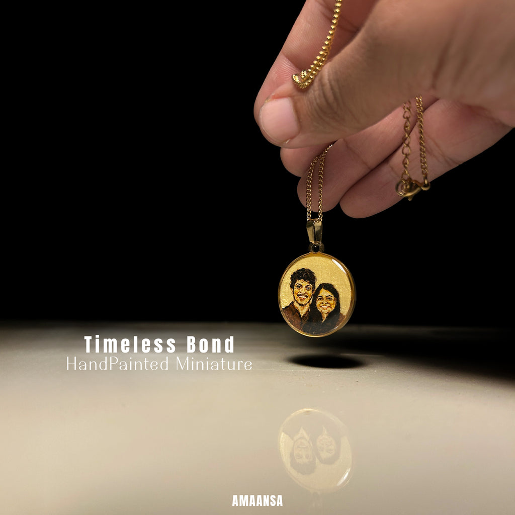 18k Gold plated pendant with a hand-painted miniature of two people, held by a hand against a black background.