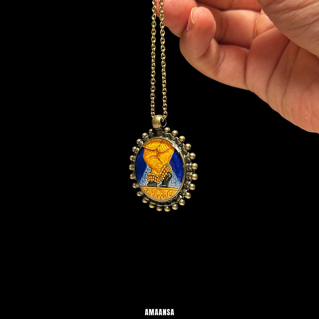 Sri Radharamanji paduka miniature pendant in brass‑tone beaded frame, devotional necklace lifted against neutral backdrop for old‑world look.