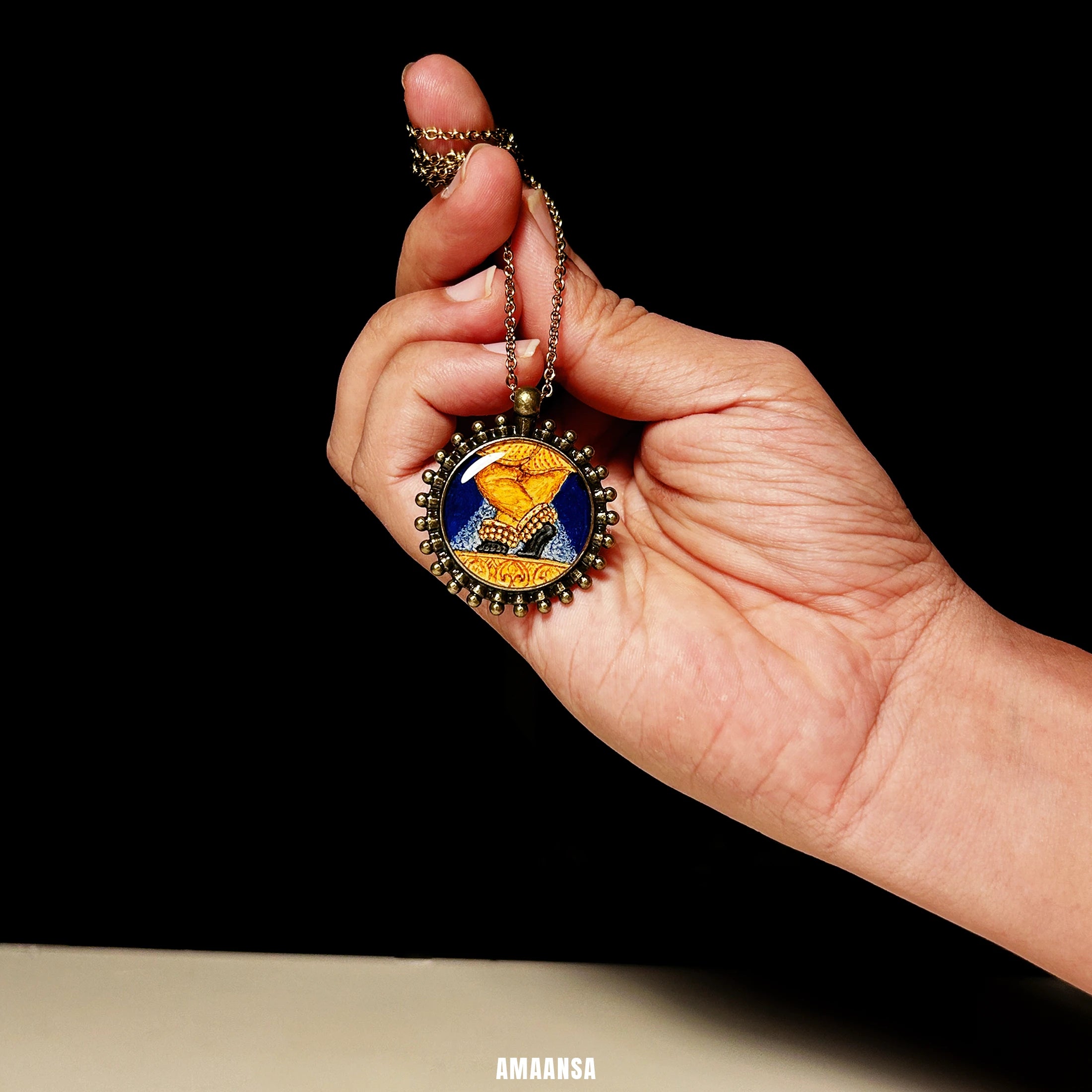 Close‑up of vintage Sri Radharamanji paduka pendant on chain, blue background and brass‑tone detailing emphasising temple‑inspired style.