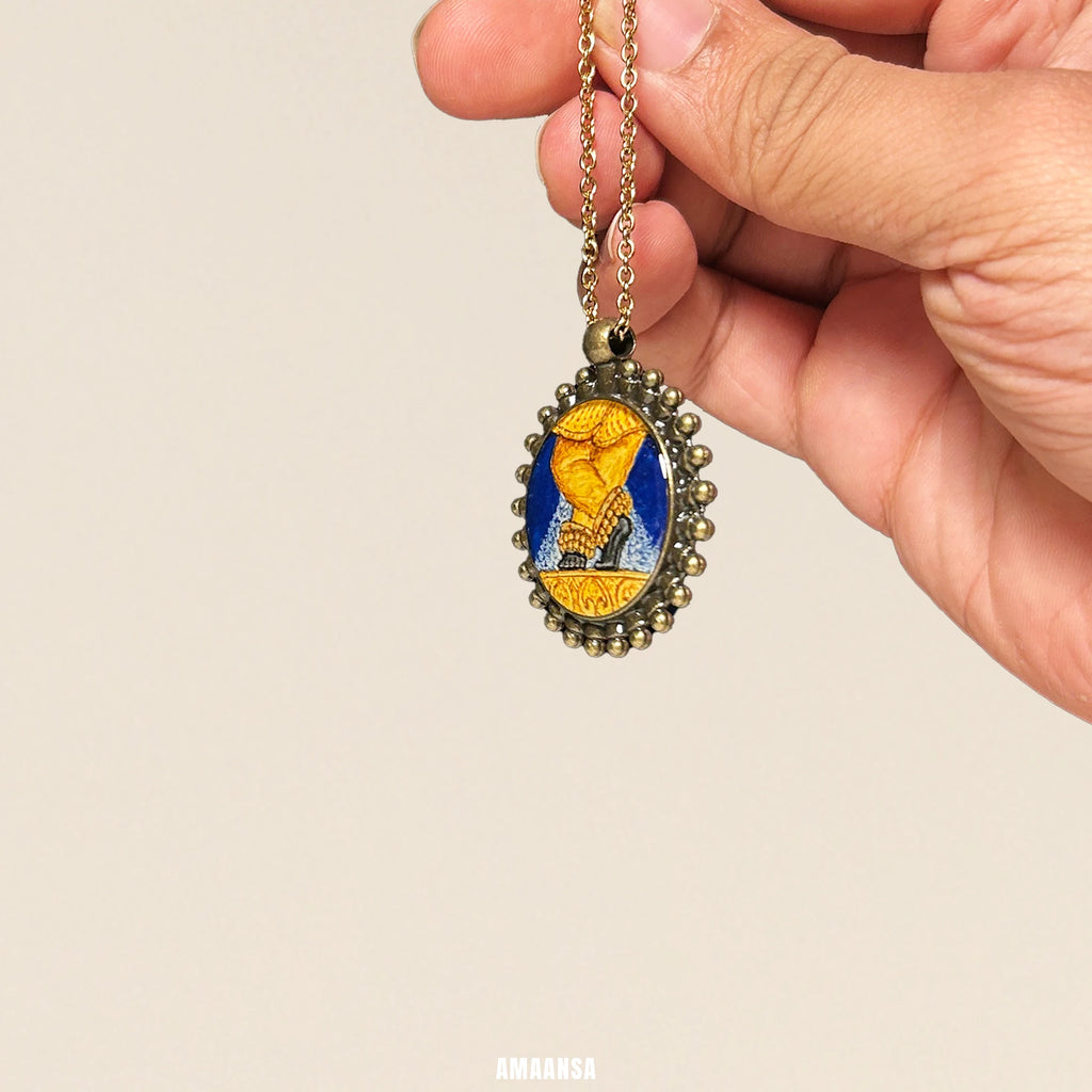 Antique brass‑tone Sri Radharamanji paduka pendant with hand‑painted feet, devotional necklace hanging against black background.
