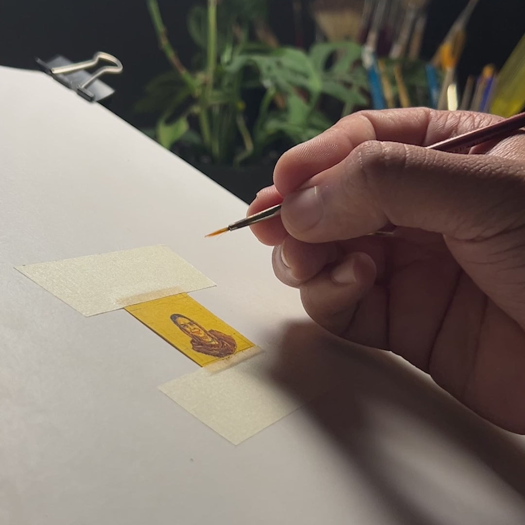 29-second studio footage showcasing custom memorial creation: artist meticulously crafting client mom's portrait with finest brush, rendering subtle details of shawl-draped hair and gentle smile on naples yellow background. Diminutive canvas secured between masking strips, surrounded by artist's tools, size reference provided by one-rupee coin. Intimate process reveals how each brushstroke preserves cherished memories in this petite legacy piece, destined for archival-quality finish.