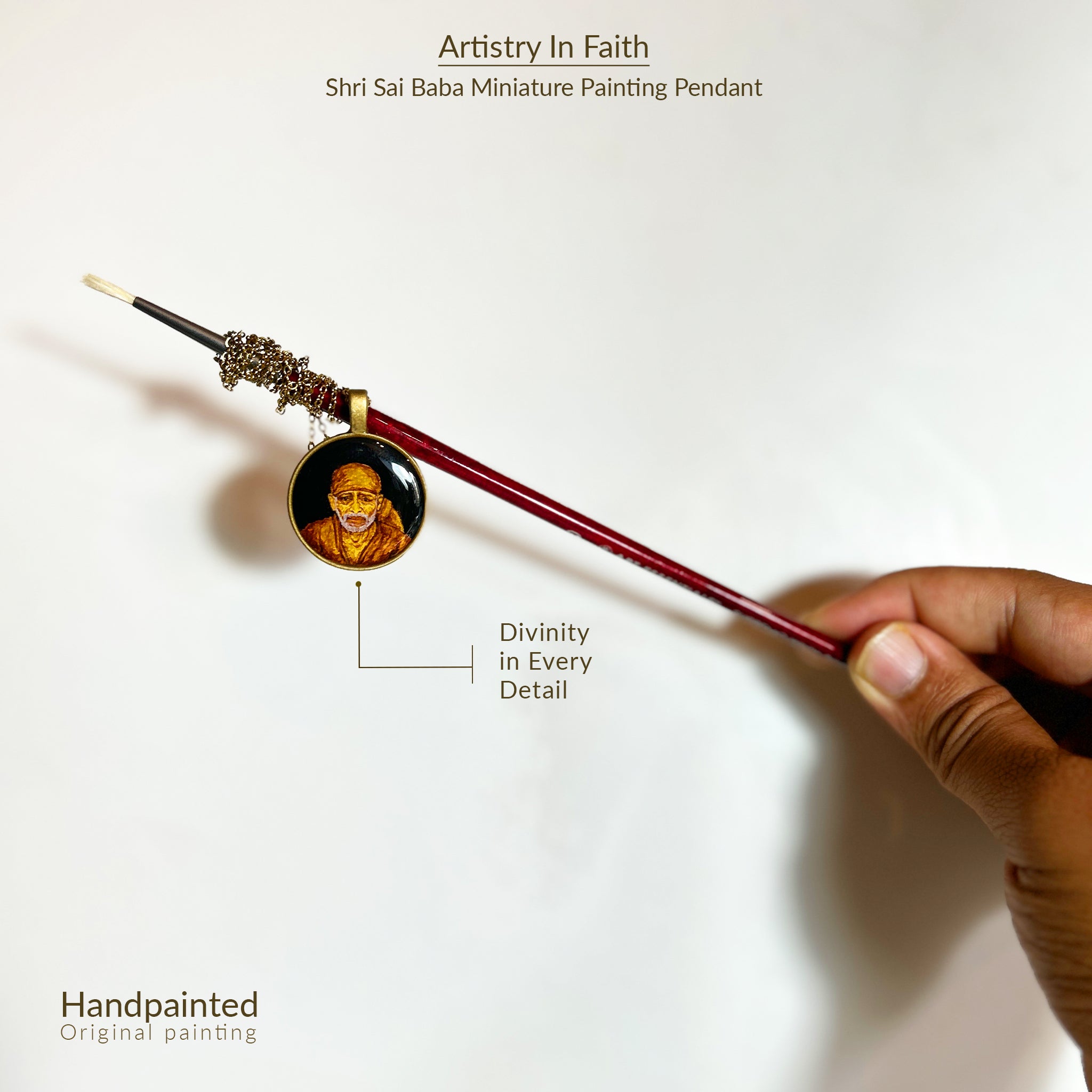 AMAANSA Fine Arts Studio presents: Sacred art pendant (26mm) showcasing Shirdi Sai Baba's divine portrait. His gentle gaze rendered with spiritual precision, framed in classic brass finish. Creatively displayed on extended paint brush handle with antique gold colored chain delicately wrapped, set against pristine white background. Sealed with protective layer, this blessed medallion exemplifies artistic devotion.