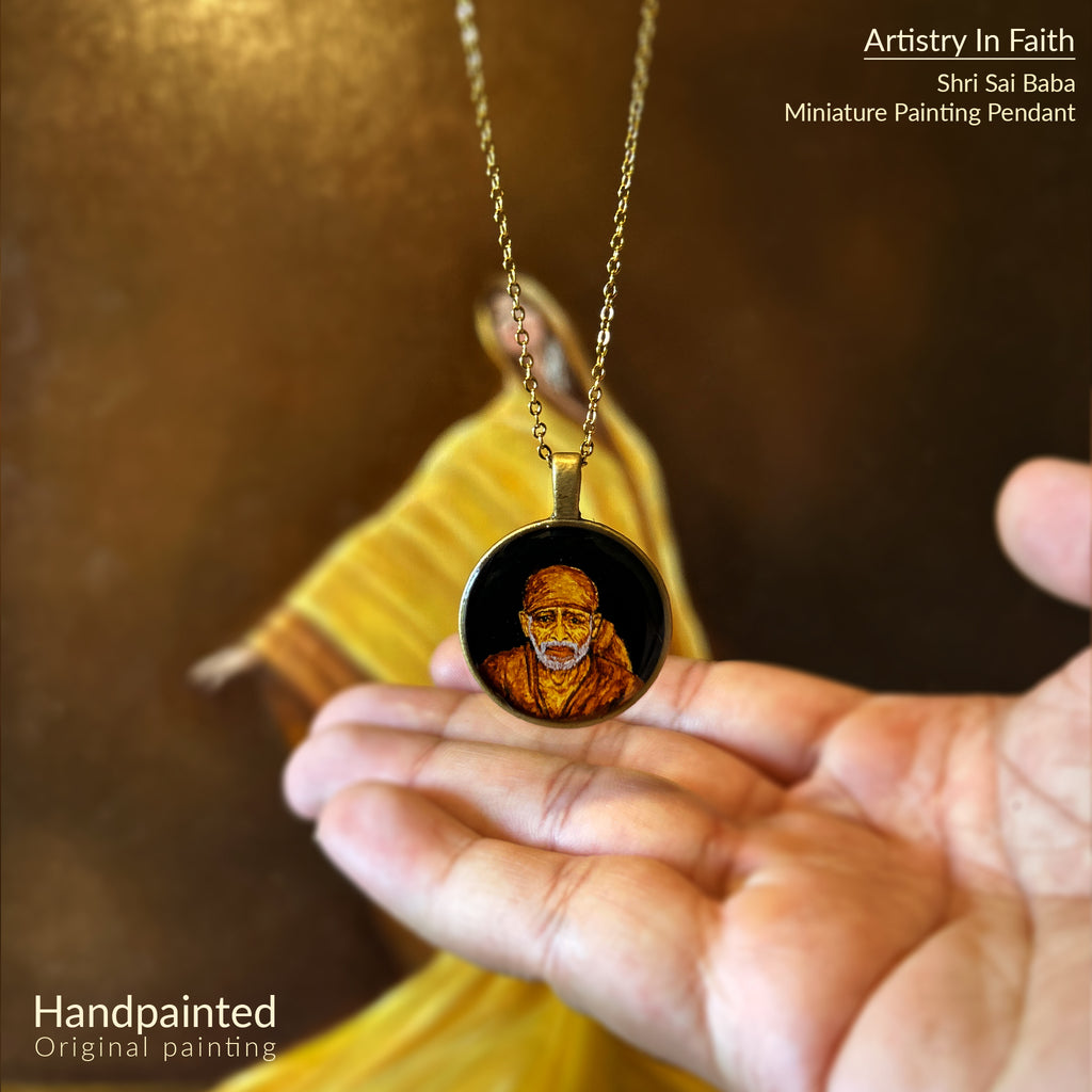 AMAANSA's sacred art pendant (26mm) featuring revered Shirdi Sai Baba's divine portrait with meticulous detail. His characteristic headscarf and benevolent expression rendered in rich earthen tones, framed by minimalist brass design. Pendant gracefully suspended above open palm with antique gold colored chain, set against artist's oil painting featuring yellow fabric. Protected by crystal-clear sealant, this blessed keepsake brings Baba's presence close to devotees.