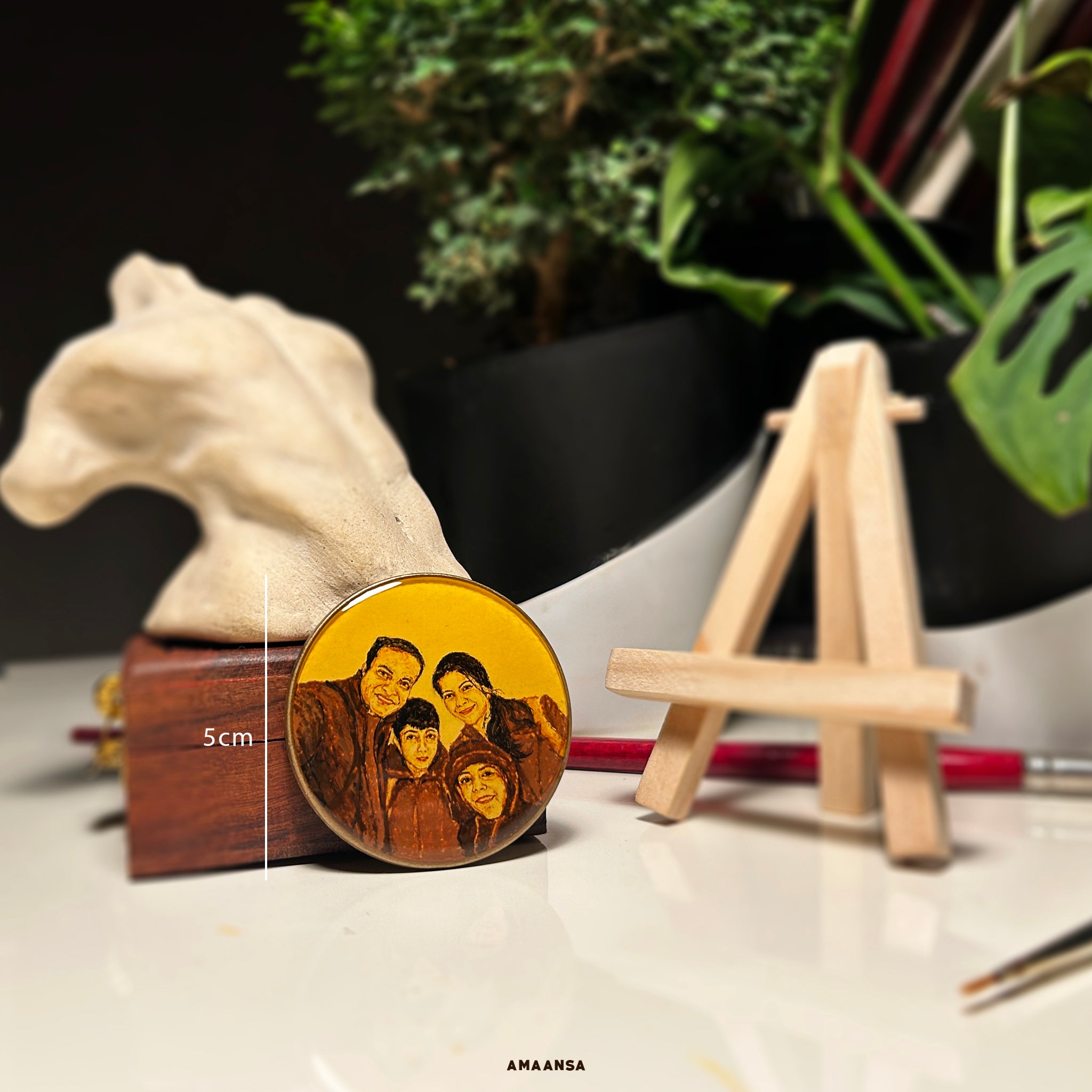 A 5cm diameter circular miniature painting on a tabletop stand, custom-painted to depict a family of four—a father, mother, and two sons—captured in a warm, vintage-hued style, naple yellow background. The intricate detail reflects the challenge of painting on such a small scale, showcasing AMAANSA Fine Arts Studio’s skill in bringing memories to life. This showpiece can be framed or displayed as-is, embodying the essence of personalized artistry crafted with precision and care.