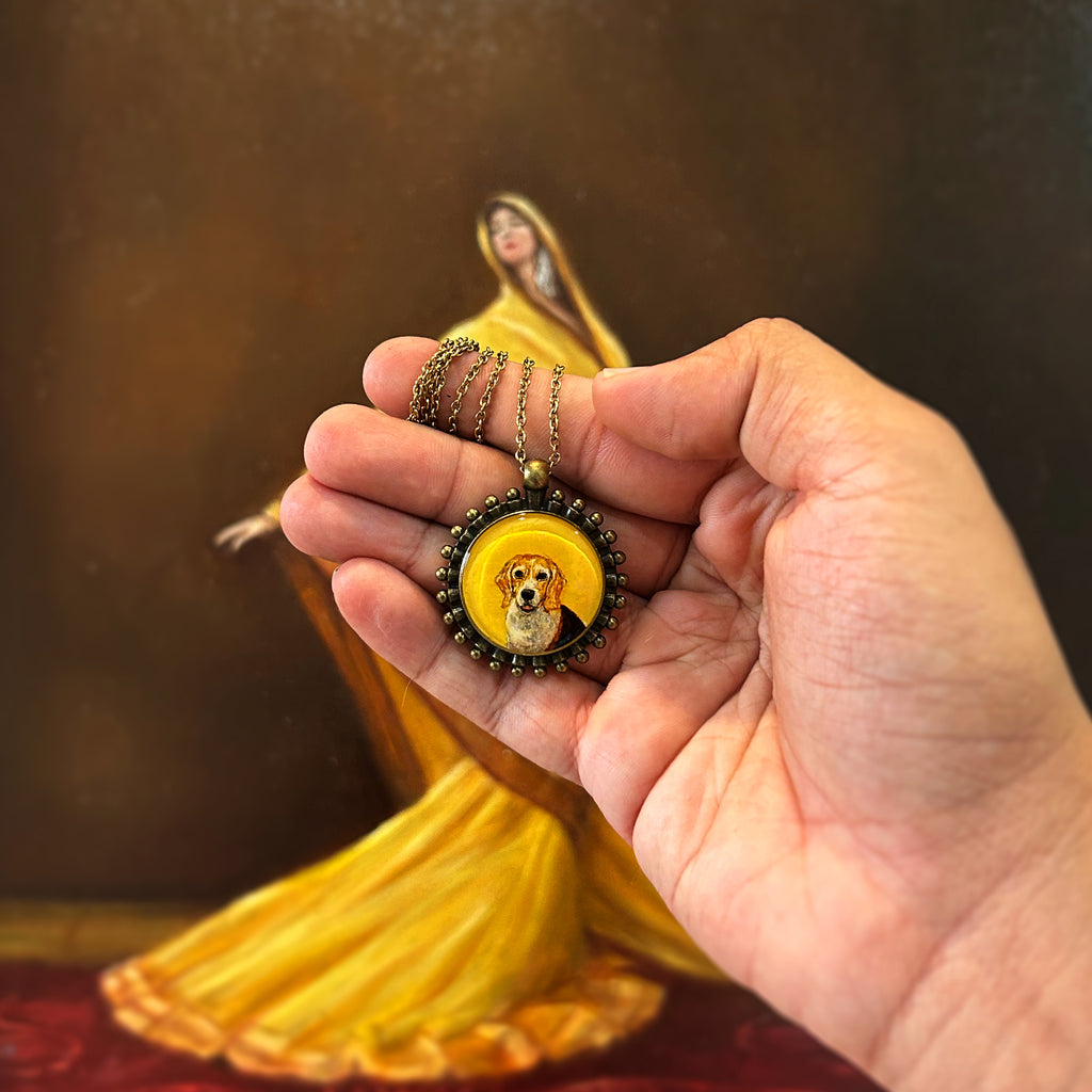Artistically rendered diminutive portrait (26mm) featuring faithful Beagle dog sweet expression, adorned with vintage-inspired Pathakkam Moti beaded frame. Treasured memory piece rests in open palm with antique gold chain gracefully coiled, photographed against ethereal yellow-draped figure creating dramatic amber ambiance. Each precious detail, from bright eyes to soft muzzle, preserved with artisan-grade finish in this forever keepsake.